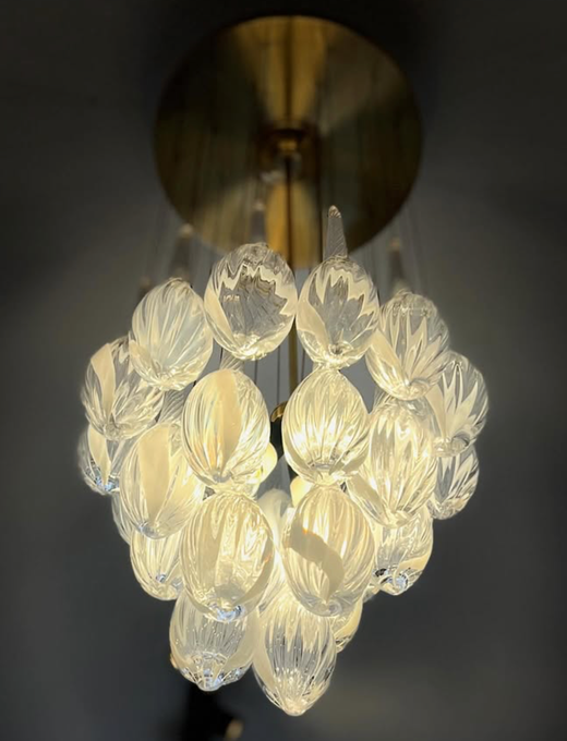 Elegante lámpara de araña con un conjunto de globos de cristal texturizados iluminados, suspendidos de una placa de techo de latón.