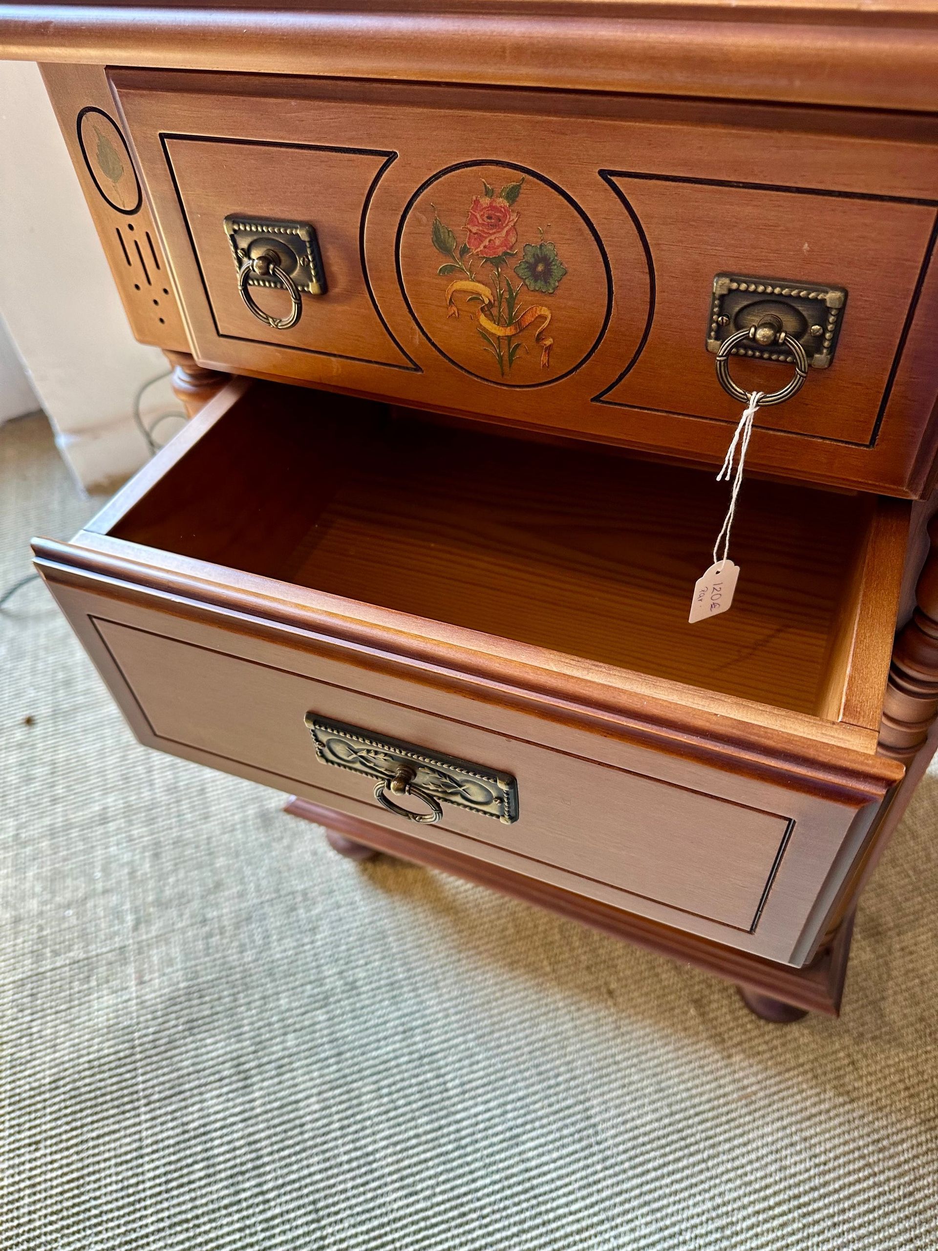 Mesita de noche de madera con dos cajones abiertos; diseño floral en el cajón superior.