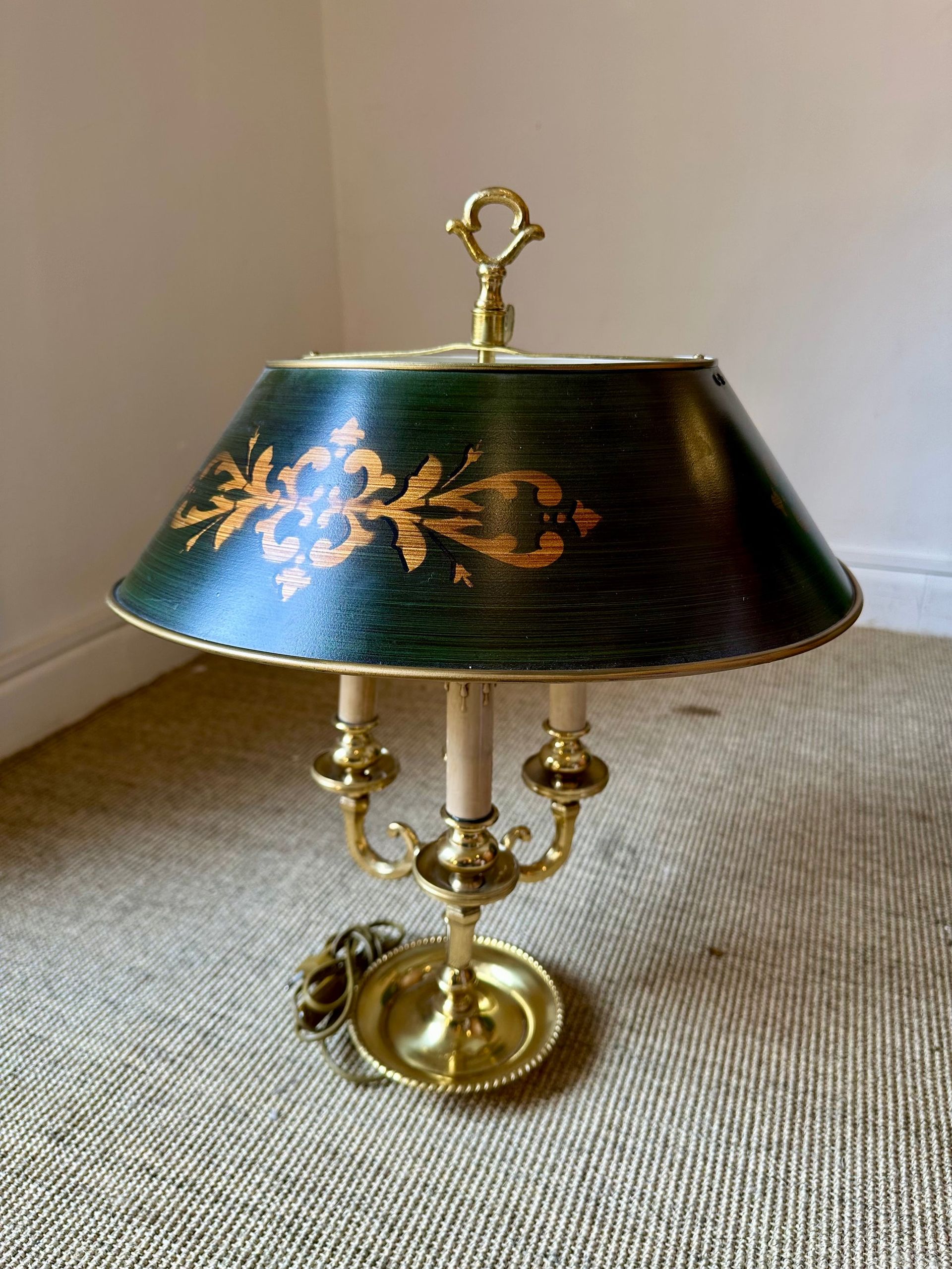 Lámpara de latón con pantalla verde y dorada, colocada sobre una alfombra.