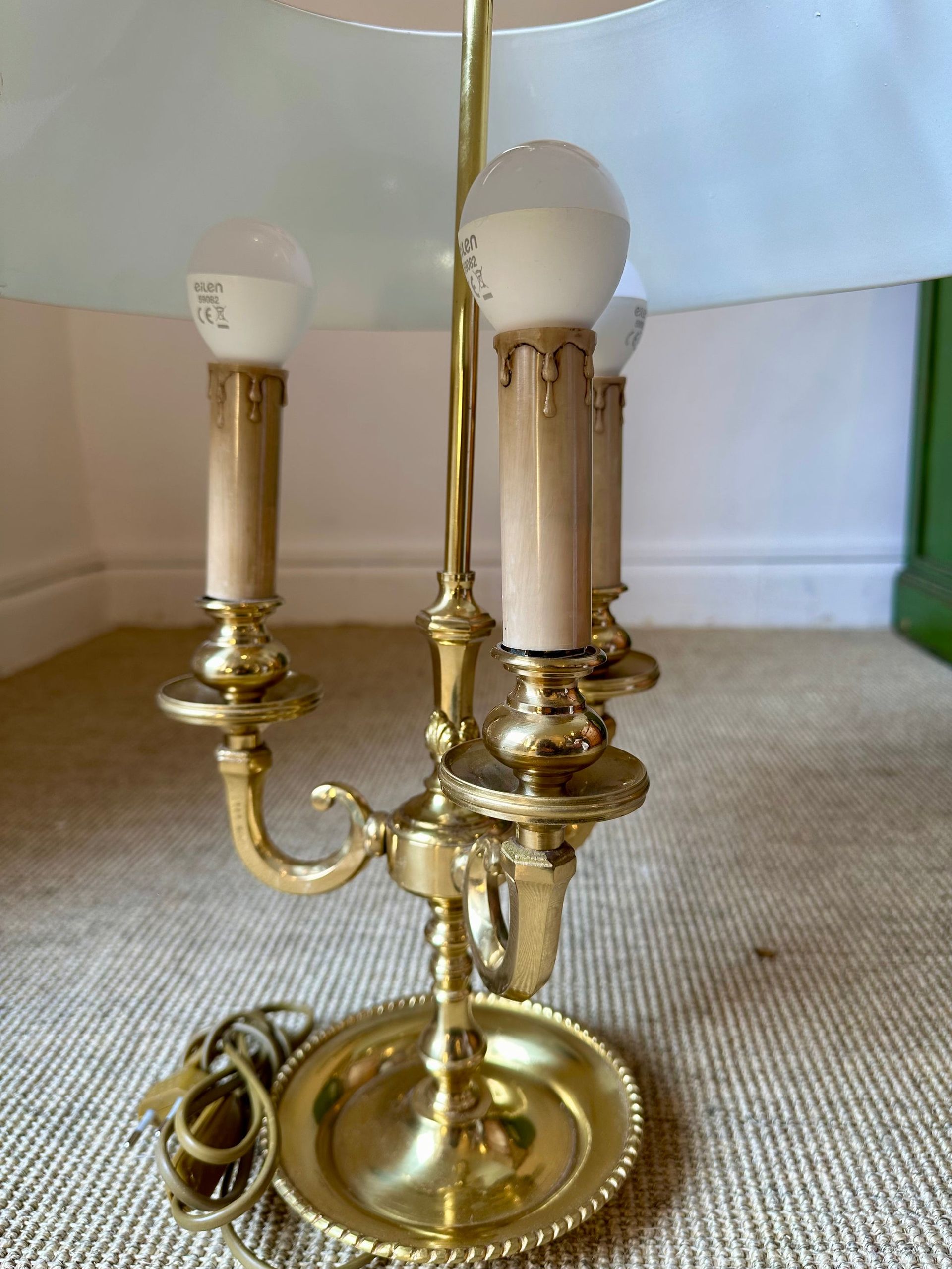 Lámpara de candelabro de latón con tres bombillas, base redonda y pantalla en una habitación.