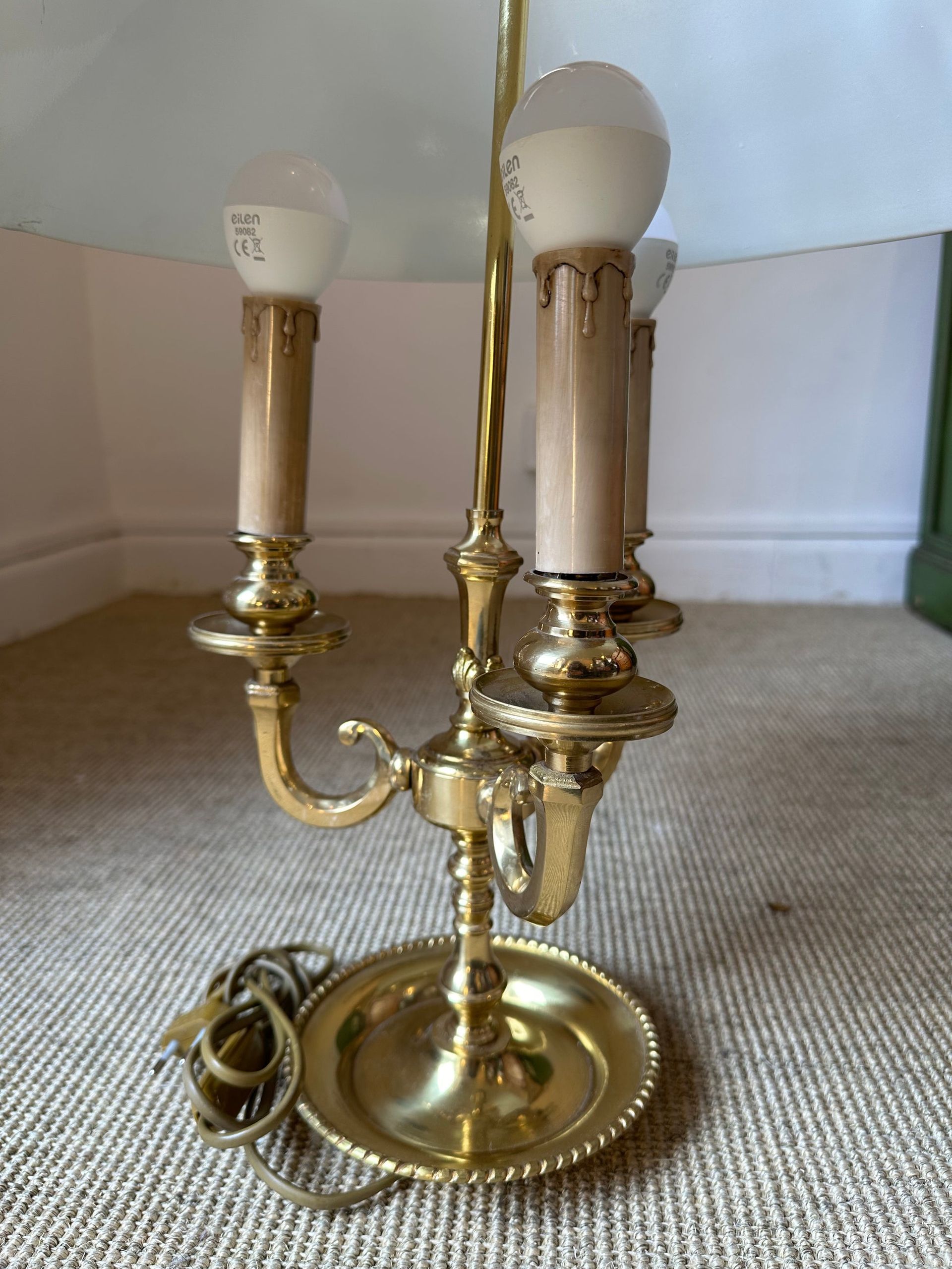 Lámpara estilo candelabro de latón con tres portalámparas y pantalla blanca, colocada sobre una superficie texturizada.