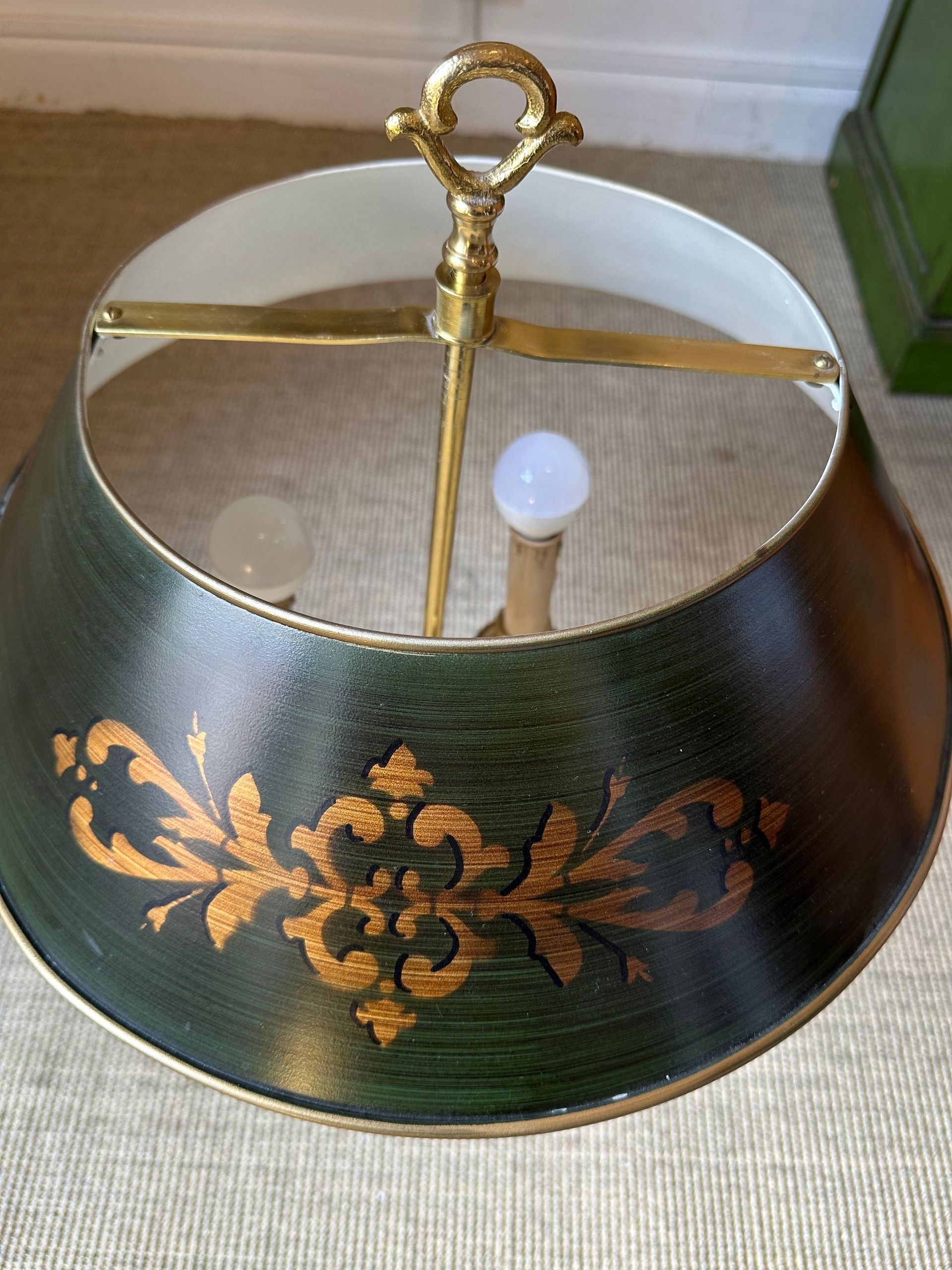 Lámpara verde y dorada con diseño de volutas decorativas.
