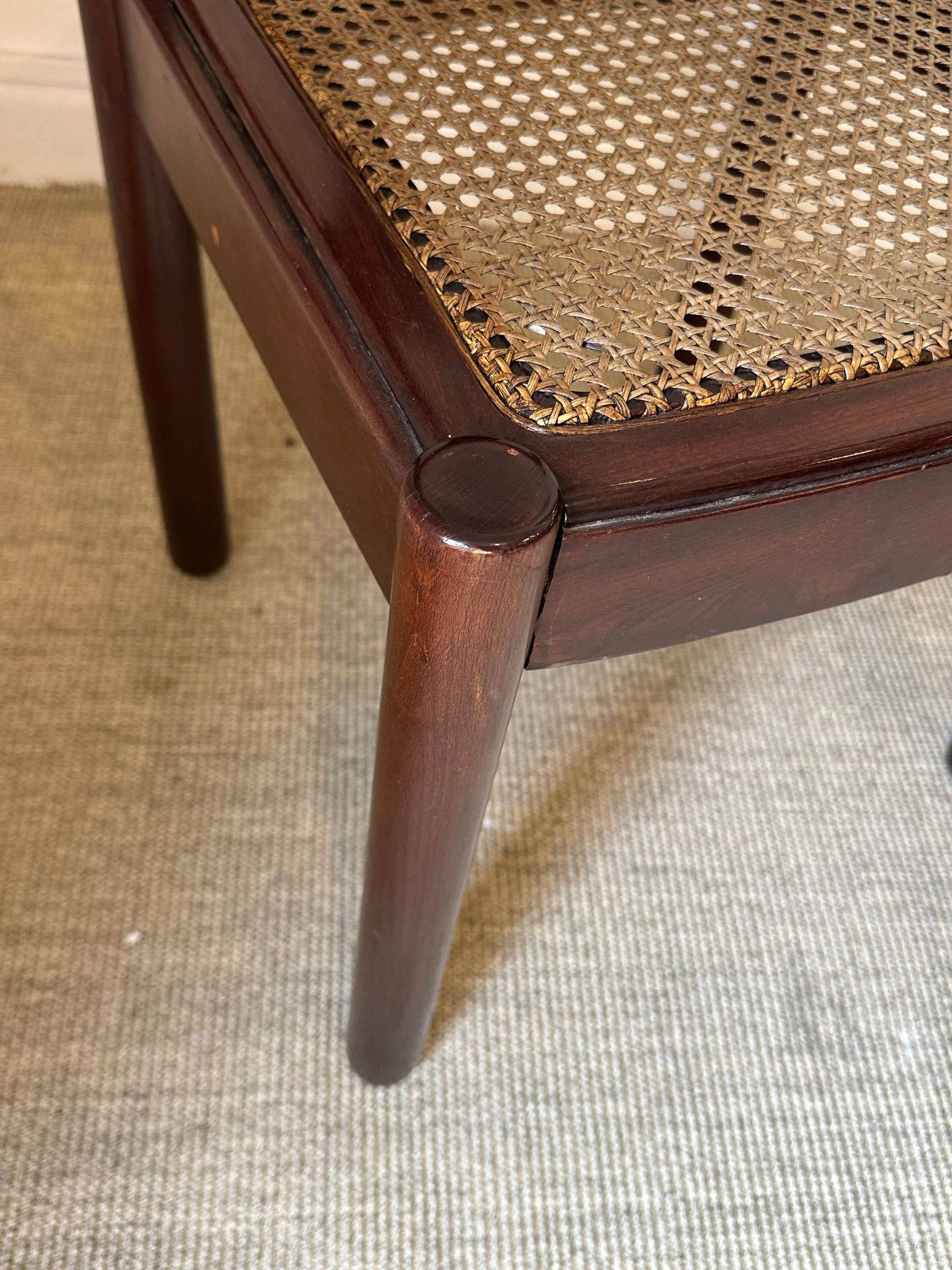 Primer plano de una silla de madera esquinera. El asiento es tejido y las patas son de color marrón oscuro sobre una alfombra beige.