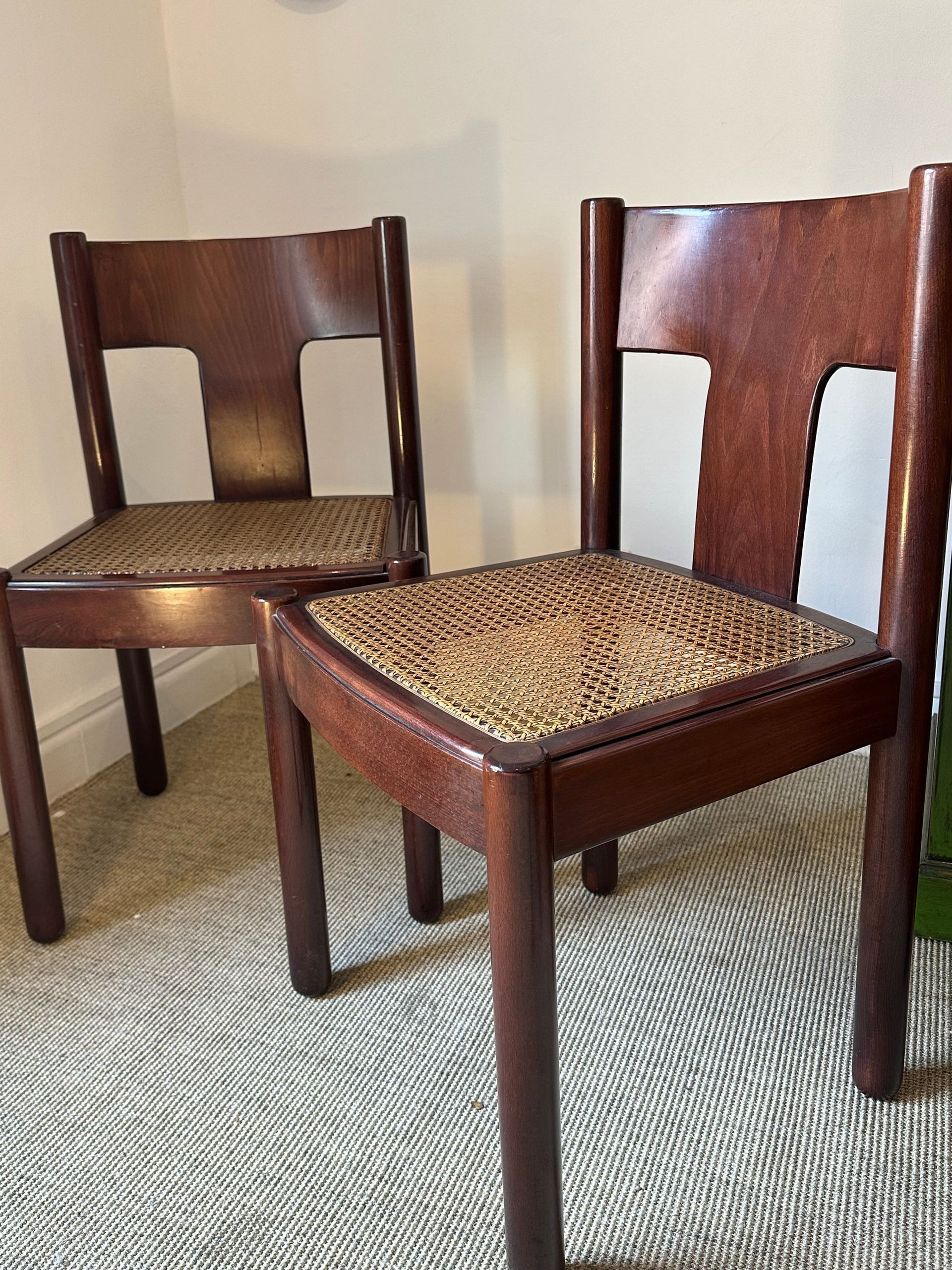 Dos sillas de madera oscura con asientos tejidos, contra una pared neutra y una alfombra.