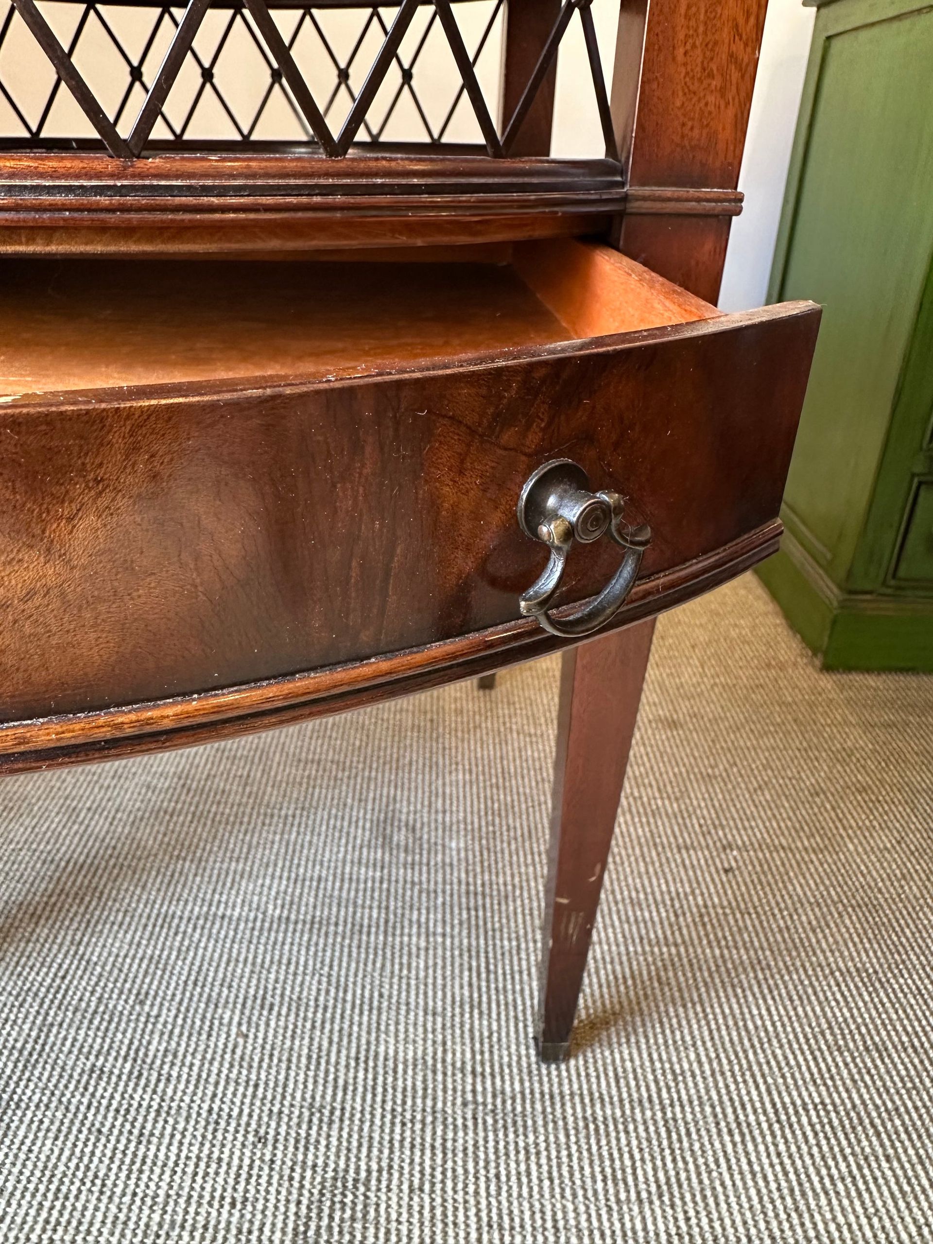 Primer plano de un armario de madera con un cajón abierto, tirador ornamentado y patas delgadas sobre una alfombra texturizada.