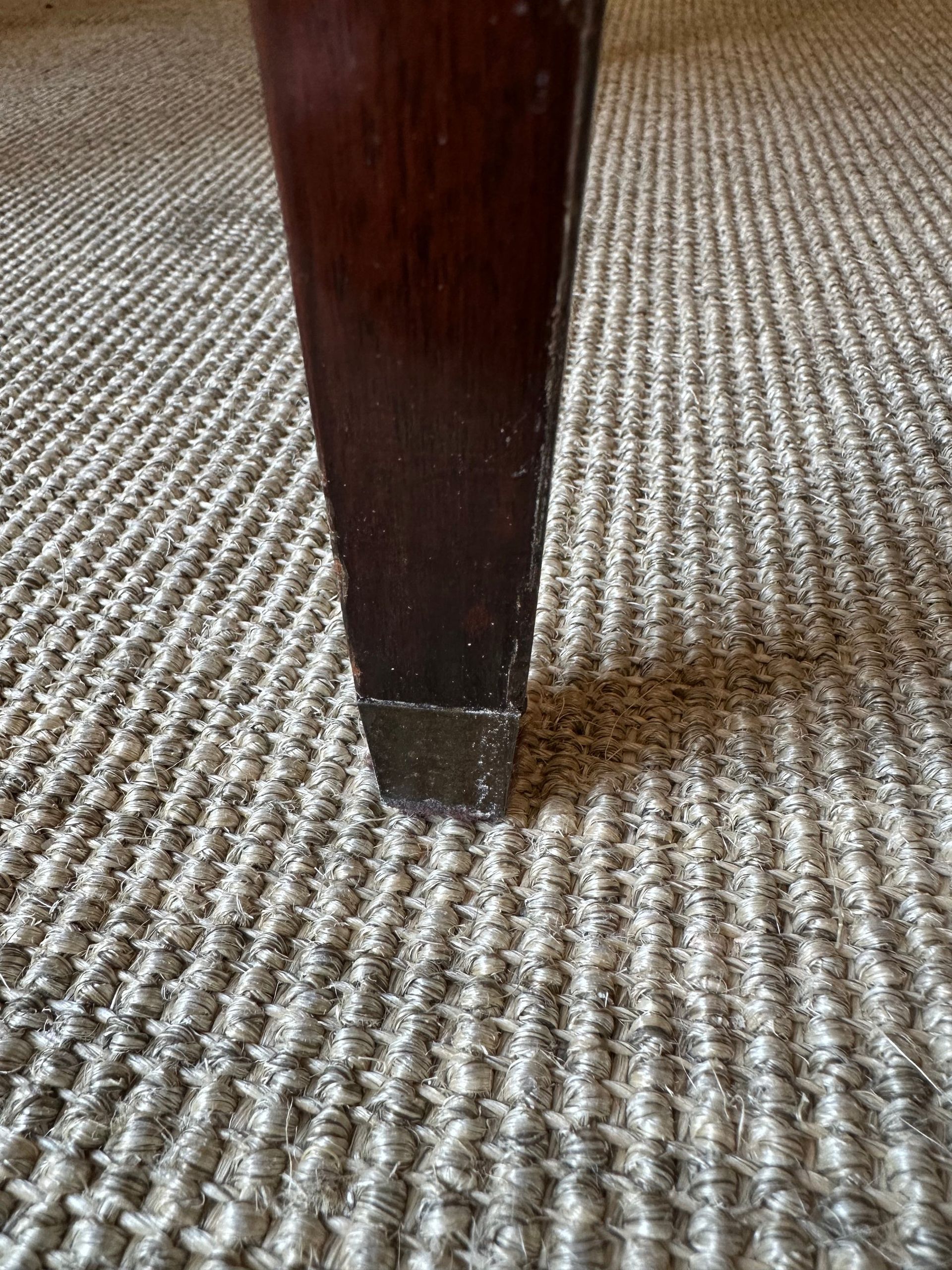 Pata de mesa de madera oscura sobre una alfombra texturizada de color neutro.