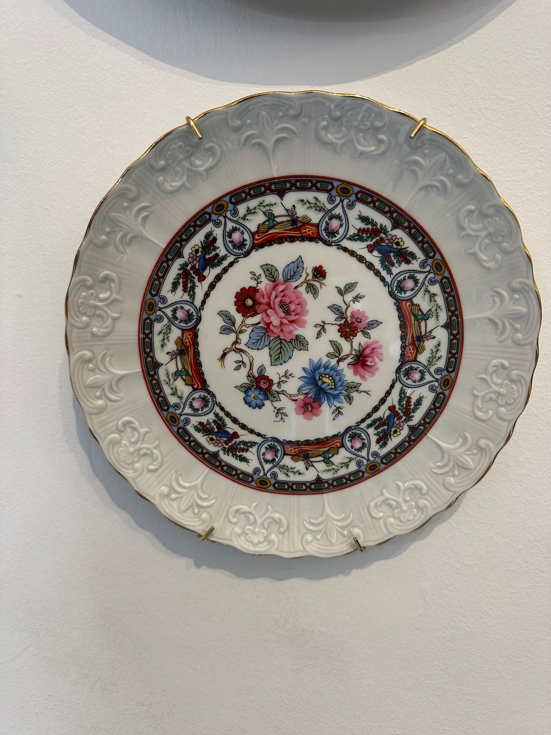 Plato decorativo de porcelana con centro floral y borde festoneado con ribete dorado.