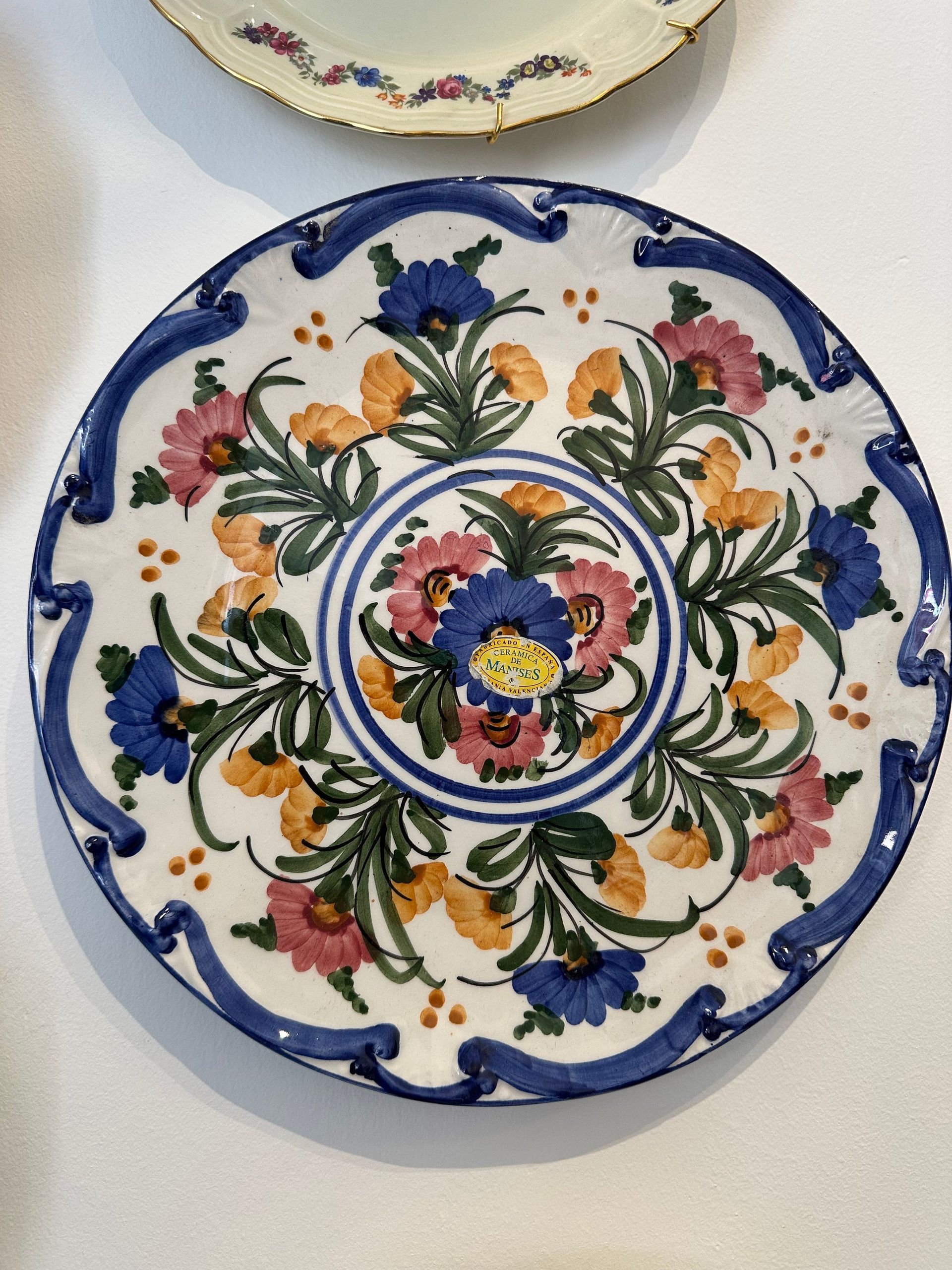 Plato decorativo de cerámica con diseño floral en tonos azules, rosas y naranjas y borde azul.