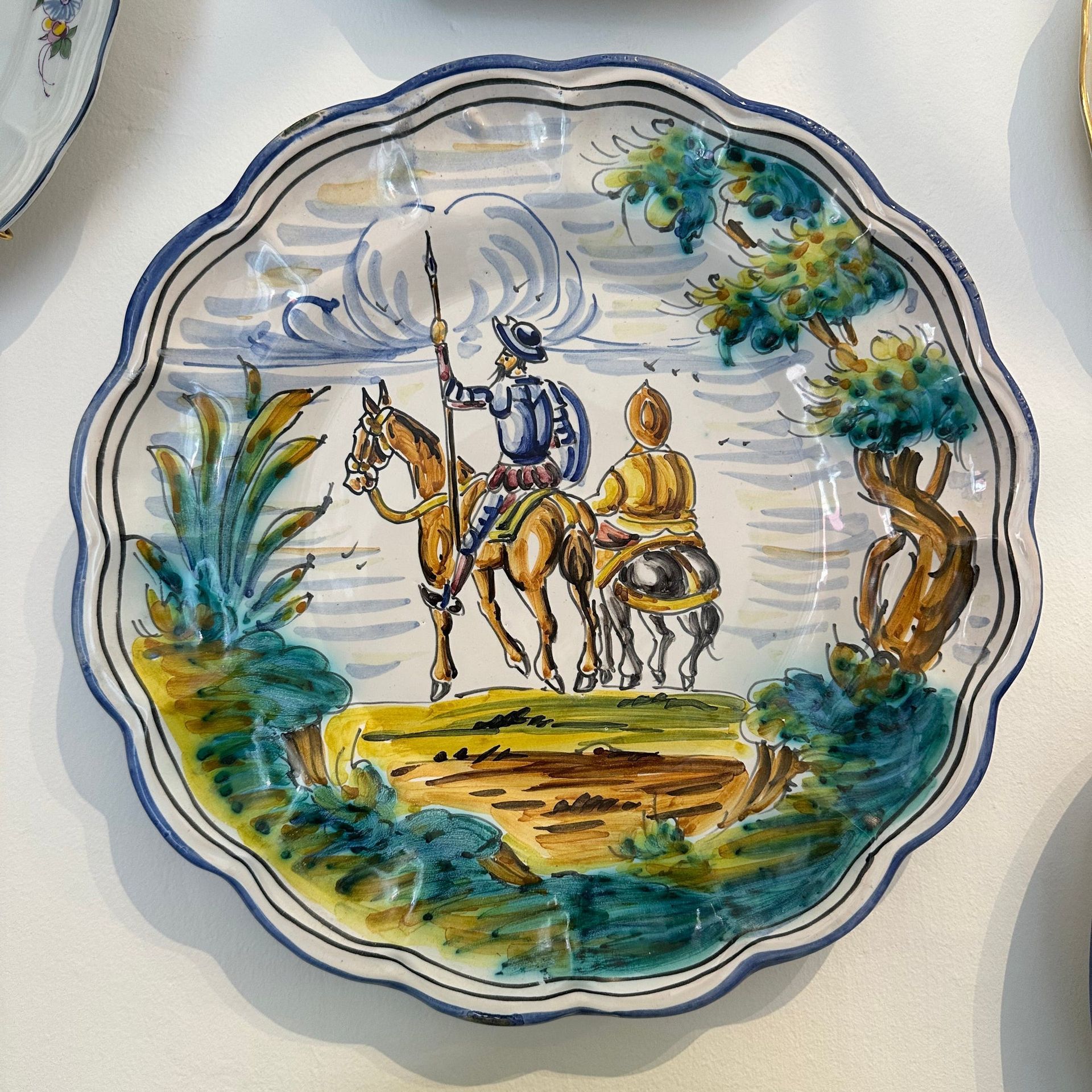 Plato decorativo con cuadro de dos jinetes a caballo en un paisaje, colores azul, amarillo y verde.