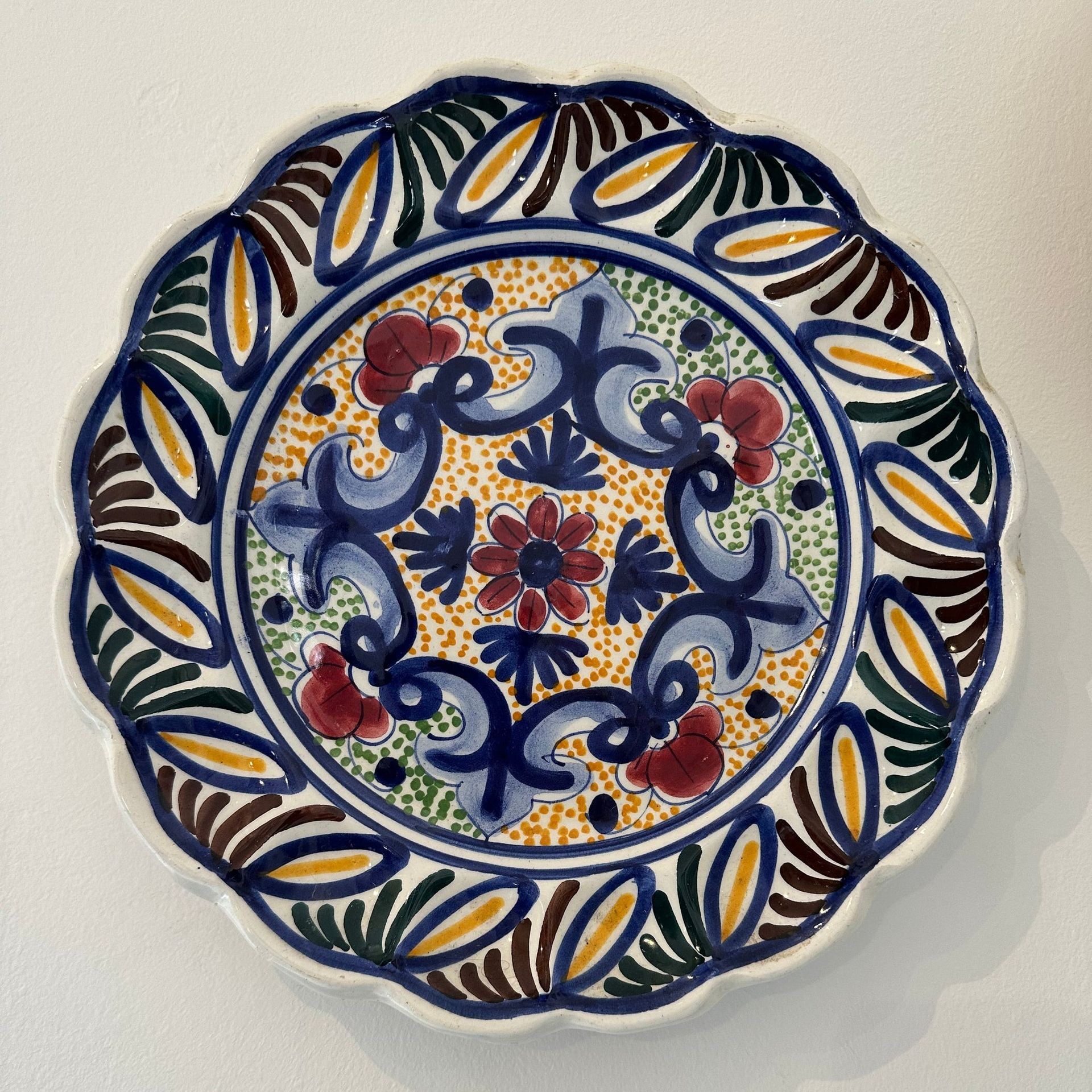 Plato decorativo de cerámica con borde festoneado, diseño floral colorido en azul, rojo y amarillo.