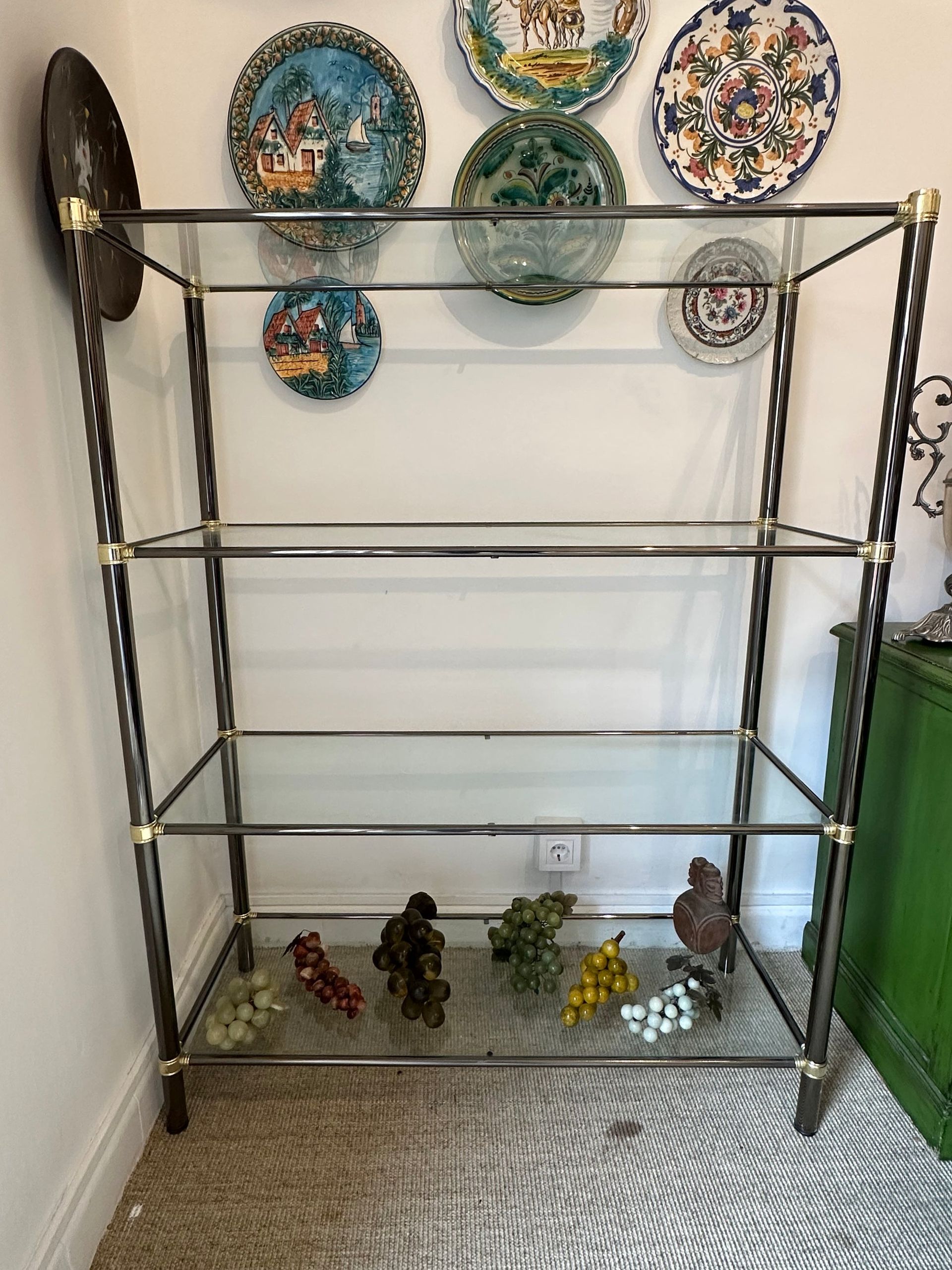 Estantería de cristal con detalles dorados, que exhibe platos decorativos y esculturas.