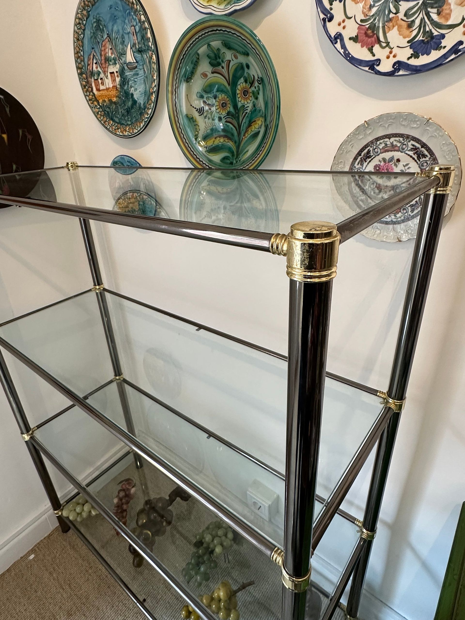 Estantería de cristal y metal con placas decorativas sobre pared blanca.