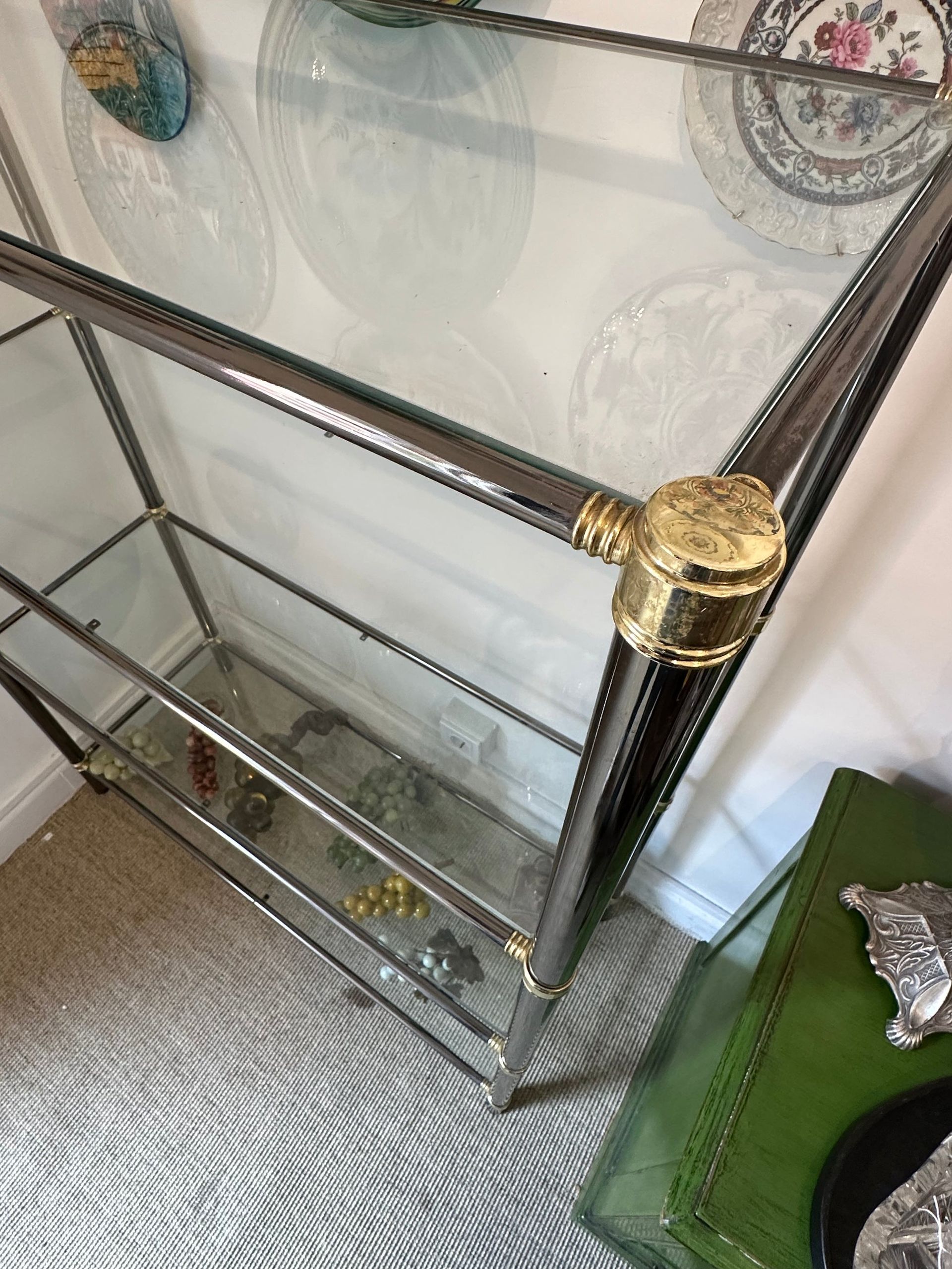 Estantería expositora de cromo y cristal con detalles dorados.