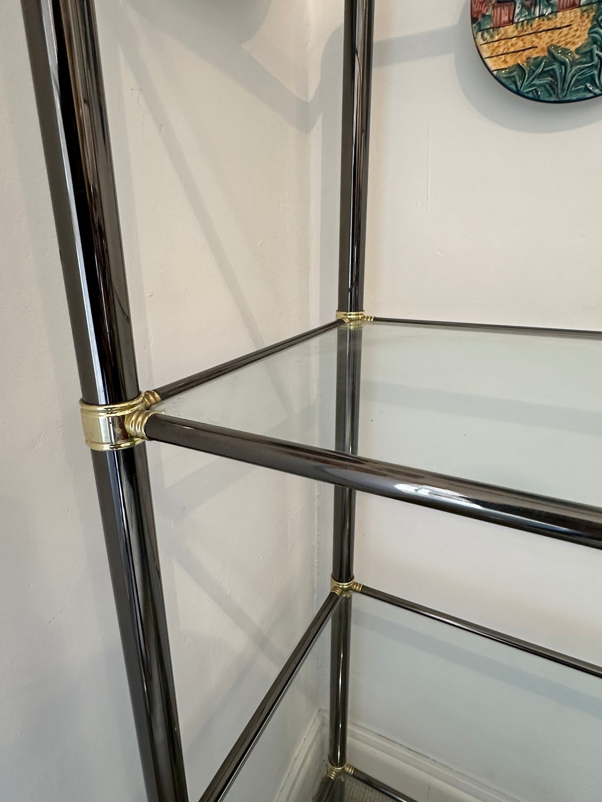 Estantería de cromo y vidrio con detalles dorados sobre una pared blanca.