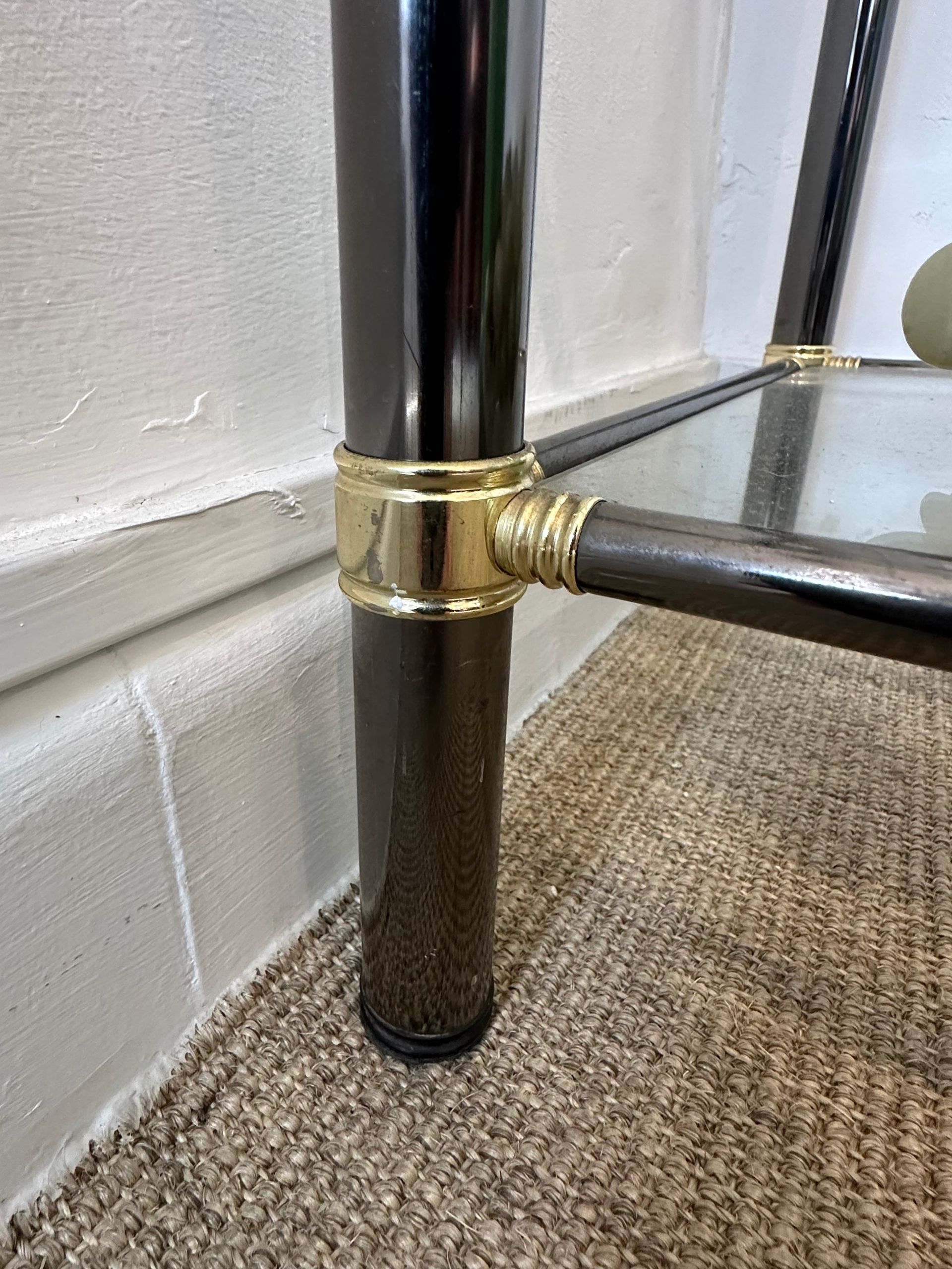 Pata de mesa de café de color negro y latón sobre una alfombra estampada junto a una pared blanca.