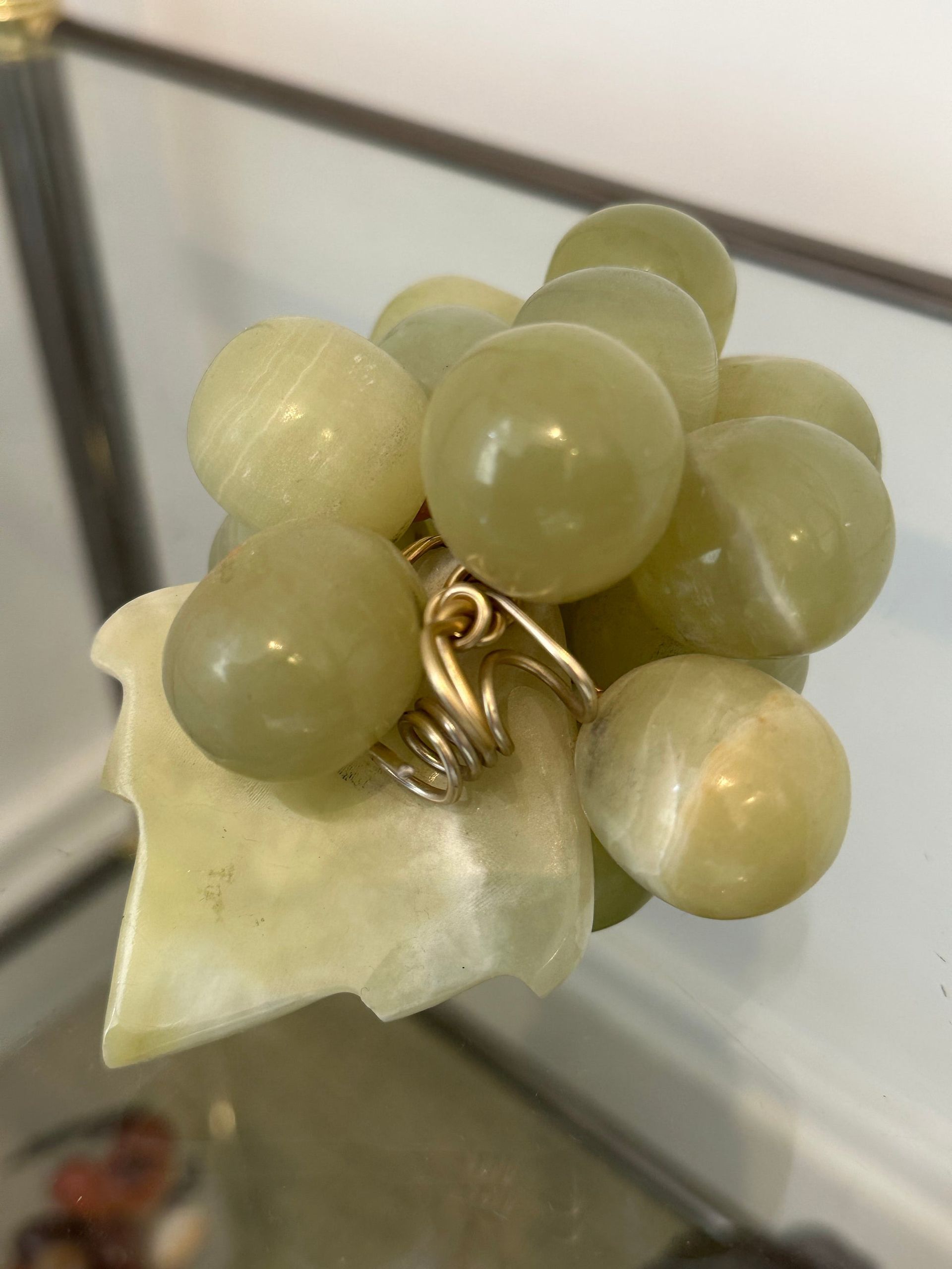 Escultura de uvas de piedra verde sobre una hoja con zarcillos de alambre dorado.