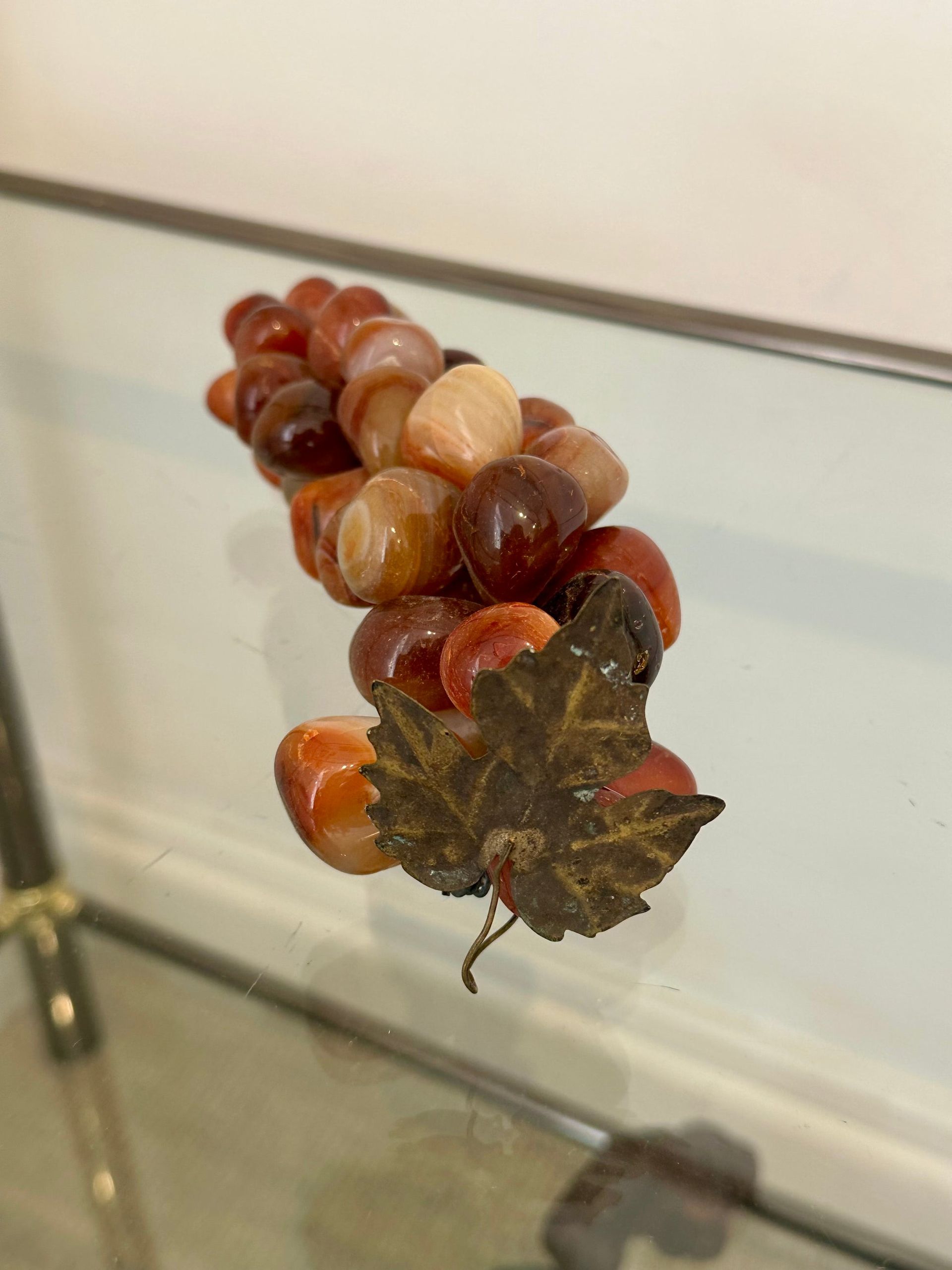 Uvas hechas de piedras pulidas, con una hoja de metal, apoyadas sobre un cristal.
