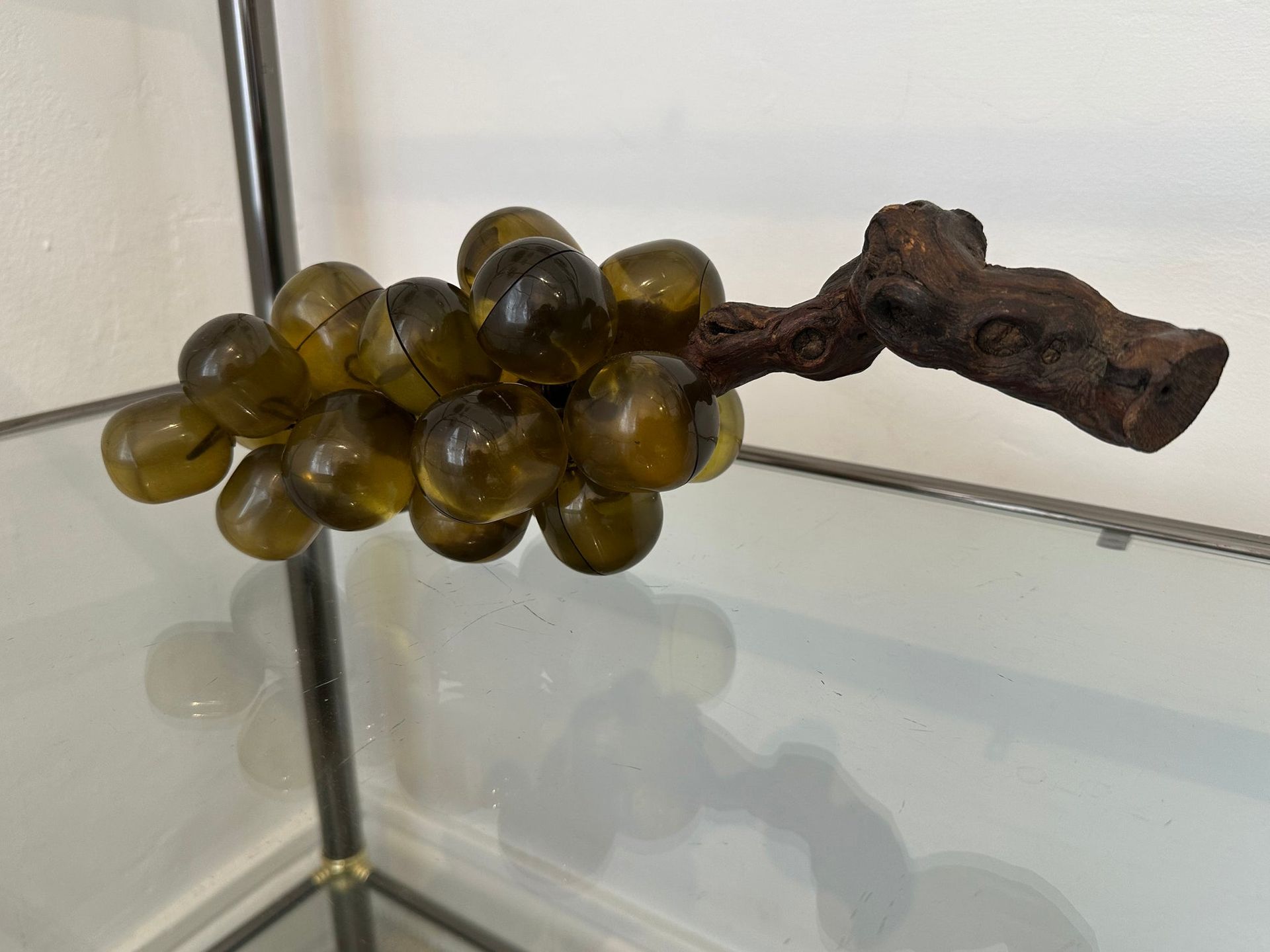Un racimo de uvas de vidrio verde unido a una vid de madera marrón, que descansa sobre un estante de vidrio.