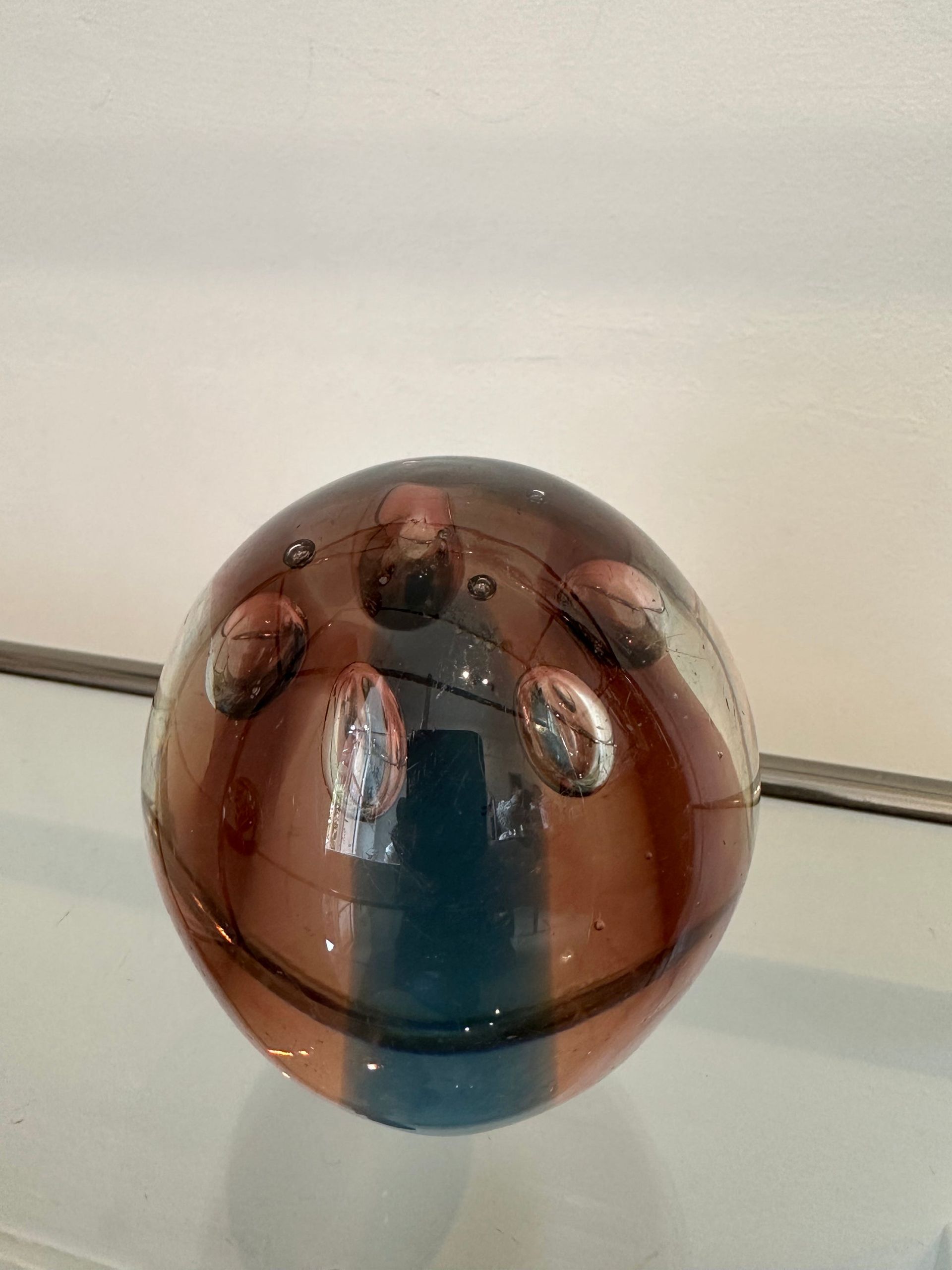 Esfera de vidrio con rayas marrones y verde azulado, acentos similares a burbujas y garabatos oscuros.