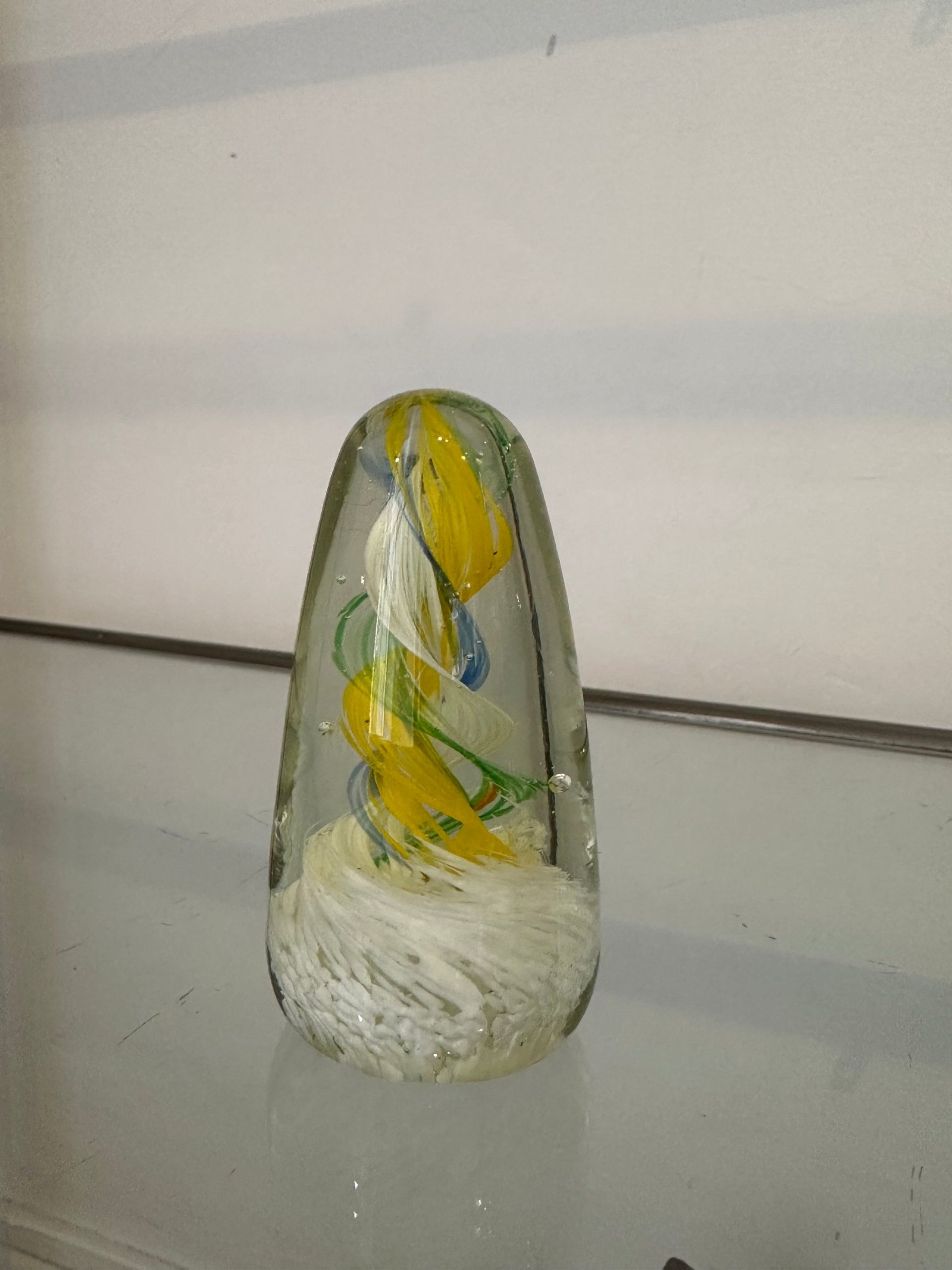 Pisapapeles de vidrio con remolinos amarillos y blancos, detalles en azul, colocado sobre un estante de vidrio.