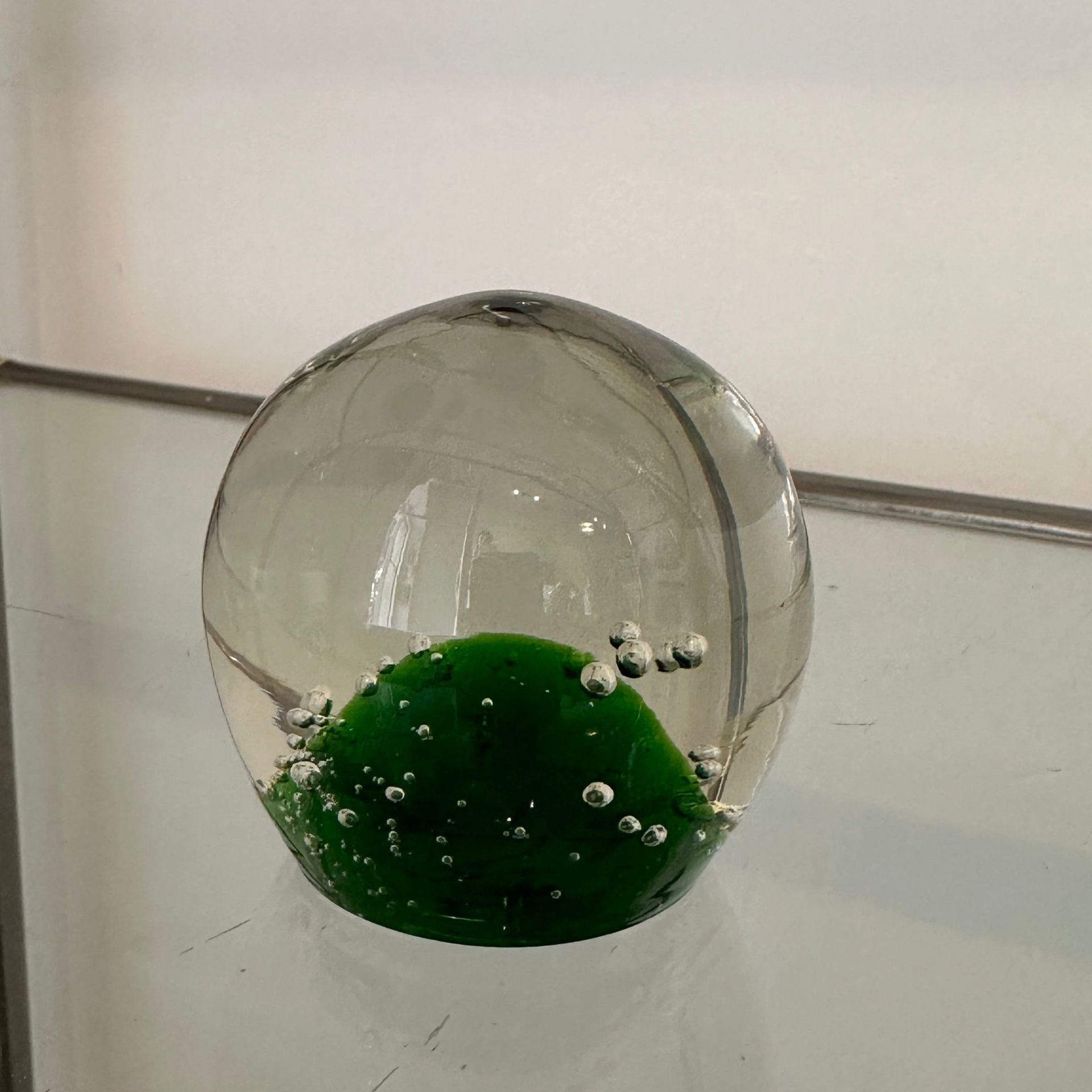 Esfera de vidrio transparente con base verde texturizada y burbujas de aire atrapadas.