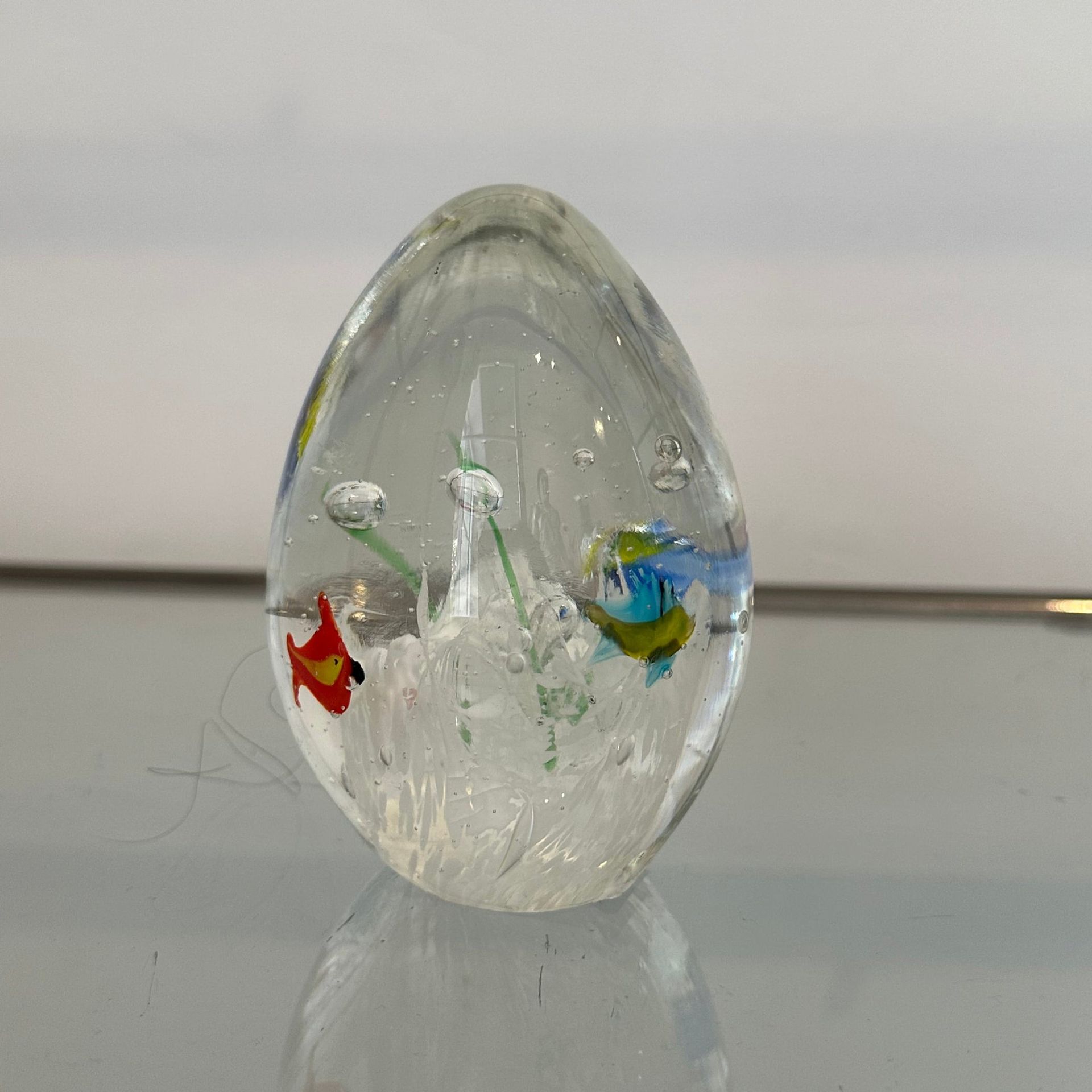 Un pisapapeles de vidrio transparente con peces de colores y burbujas en su interior.