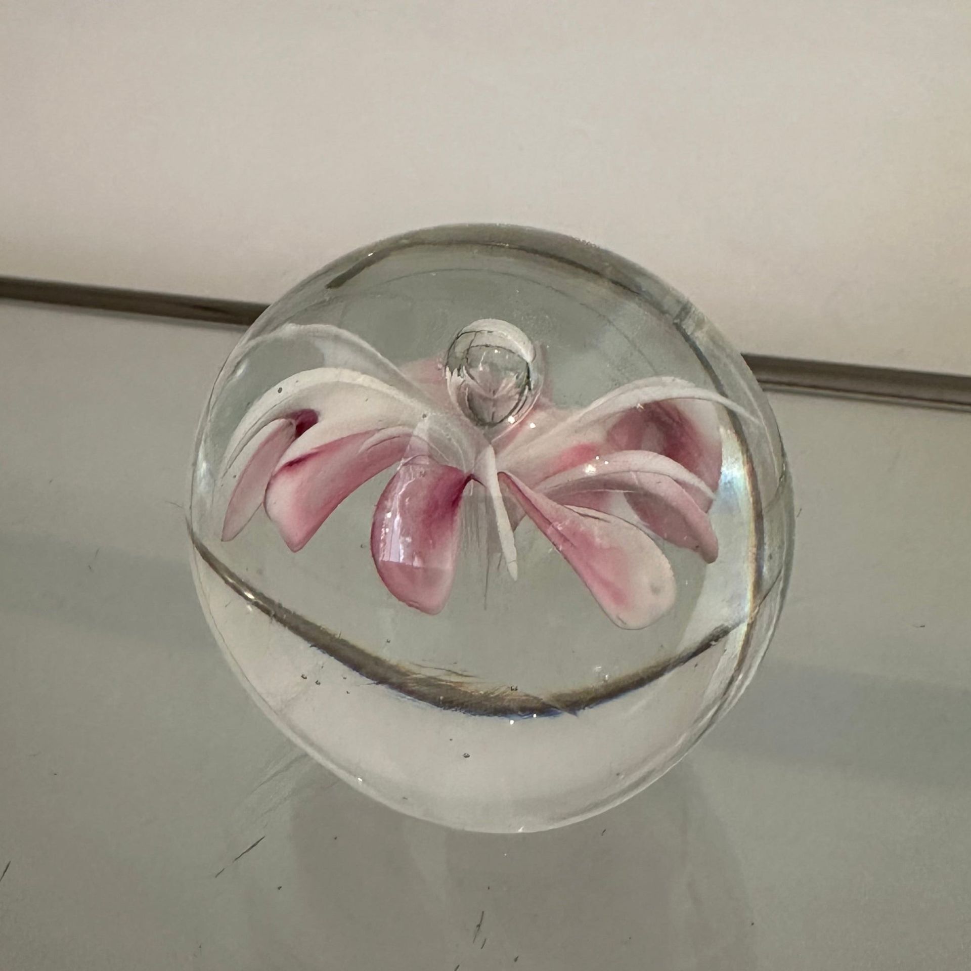 Pisapapeles de cristal con una flor rosa y blanca en su interior.