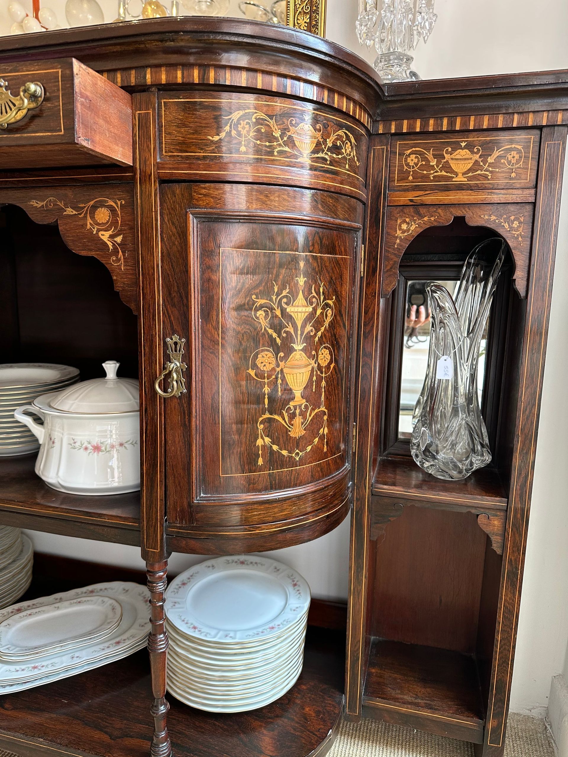 Gabinete antiguo de madera con intrincado diseño de incrustaciones, que contiene platos y elementos decorativos.
