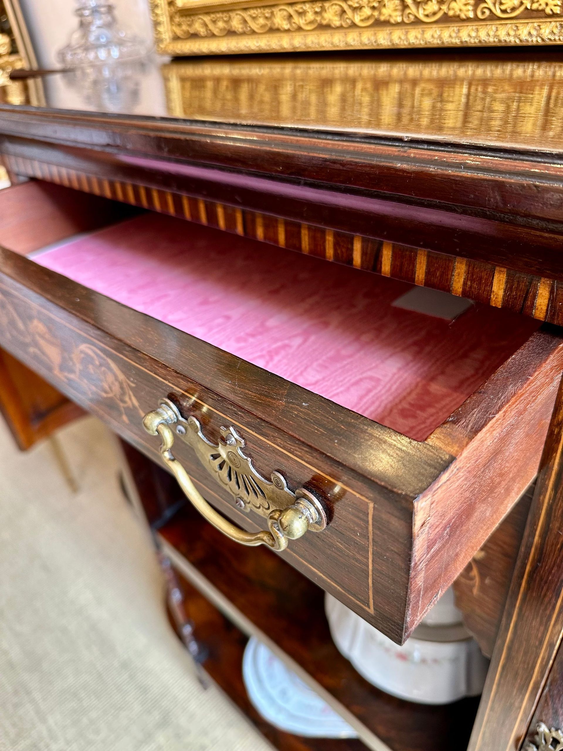 Cajón abierto en mueble antiguo de madera, interior rosa, tirador y borde dorado ornamentado.