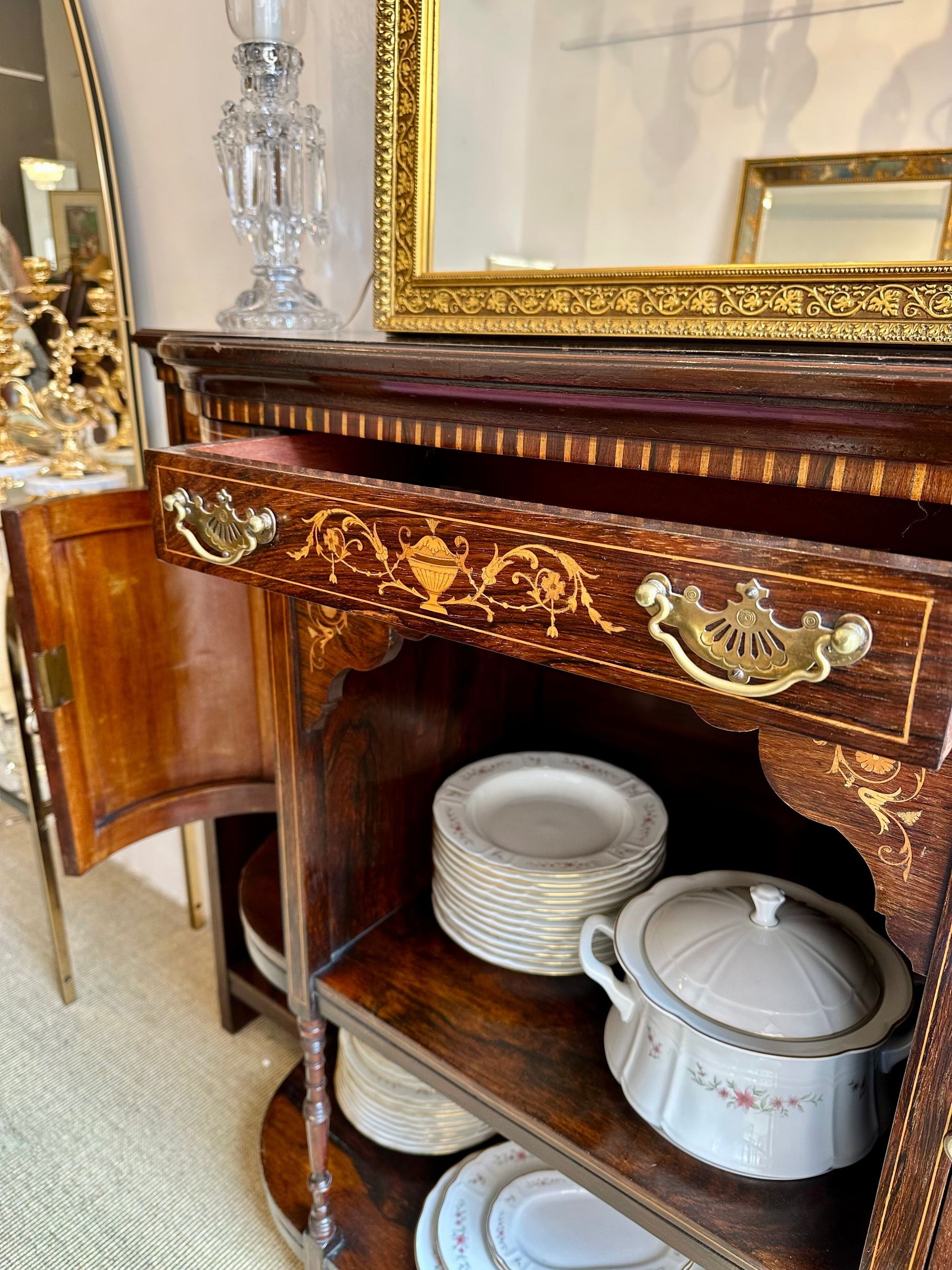 Mueble de madera con cajón abierto, herrajes dorados, platos apilados y plato con tapa.