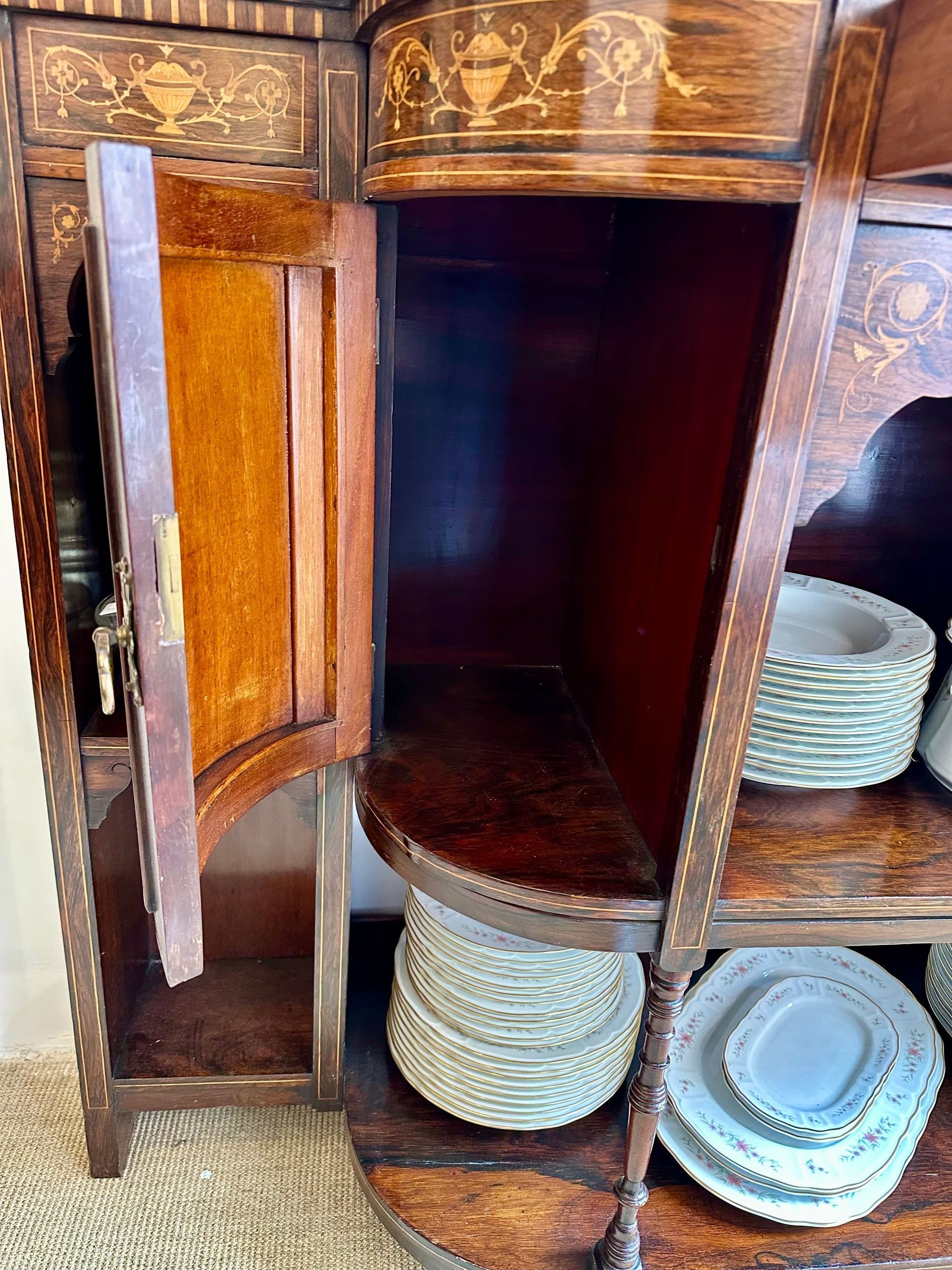 Armario de madera con puerta abierta, estantes que sostienen platos; diseño intrincado con incrustaciones en la parte superior.