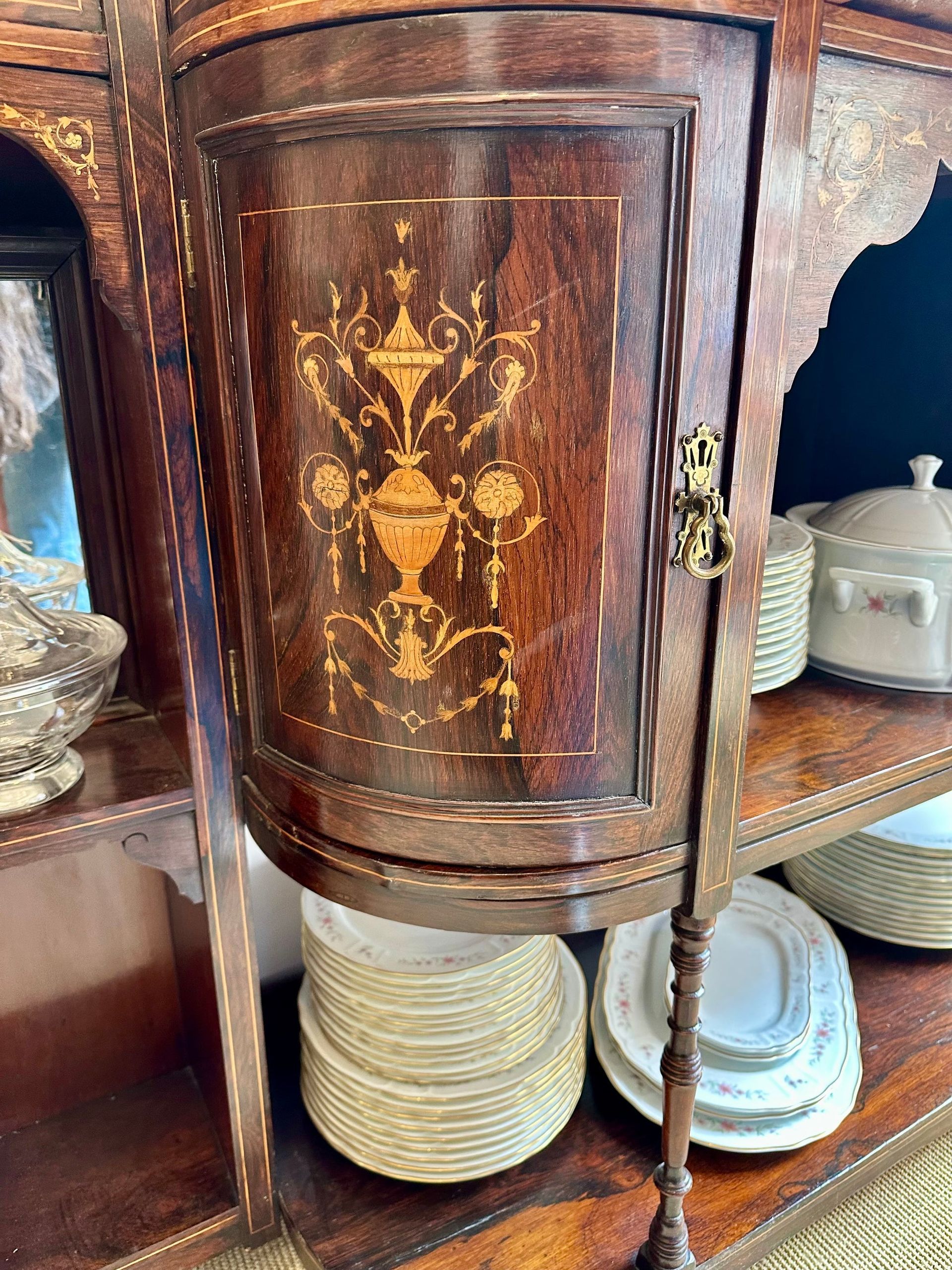 Armario esquinero de madera con diseño incrustado en la puerta, que contiene platos apilados y una pequeña cerradura.