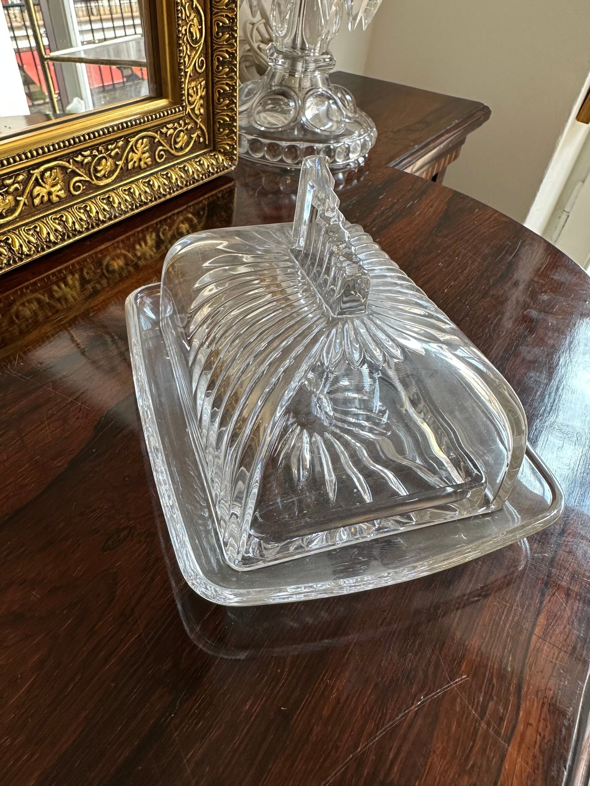Mantequera de cristal con tapa, sobre mesa de madera oscura.