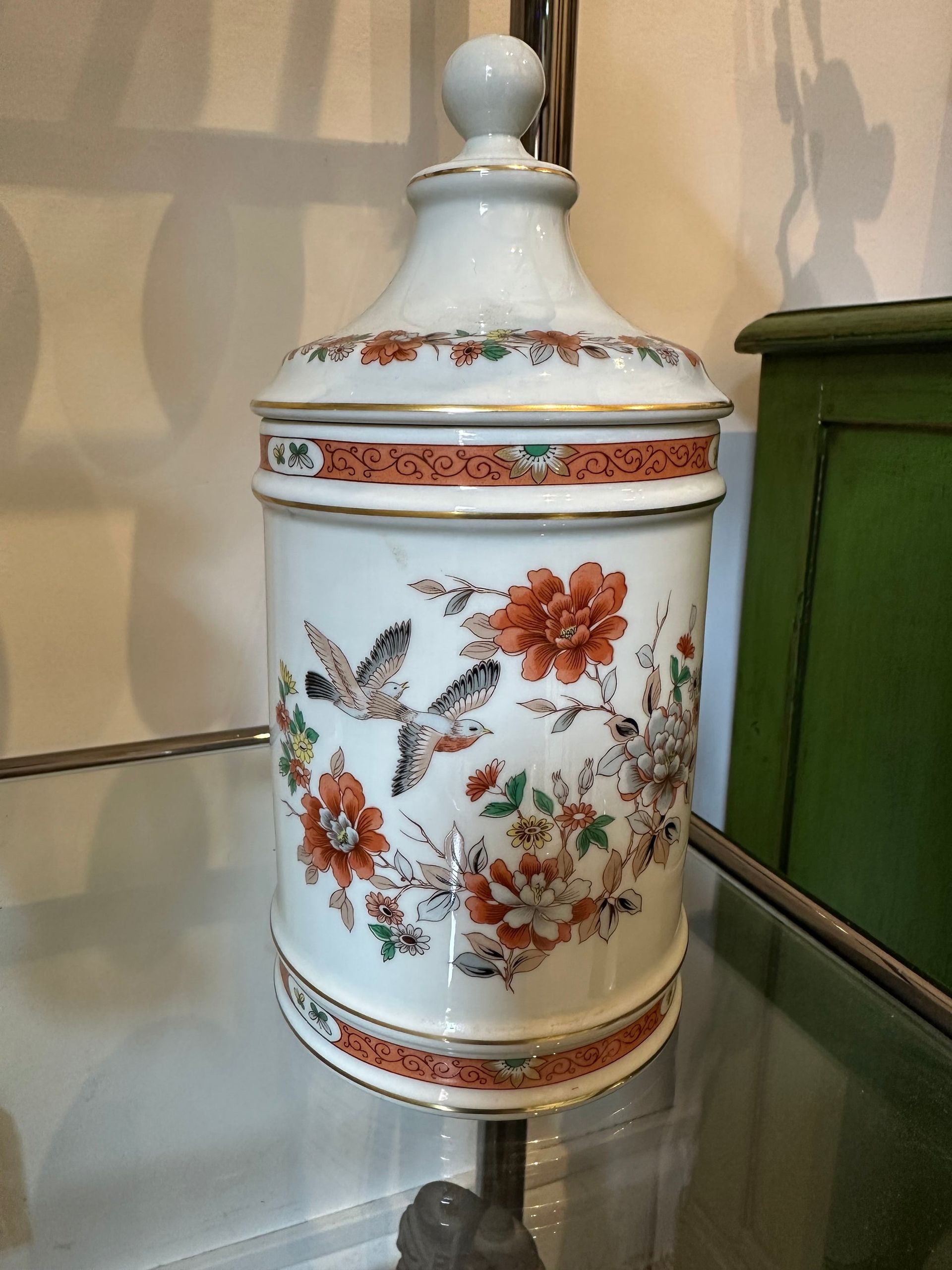 Tarro de cerámica blanca con diseño floral y de pájaros, ribete en naranja y dorado, tapa con pomo.