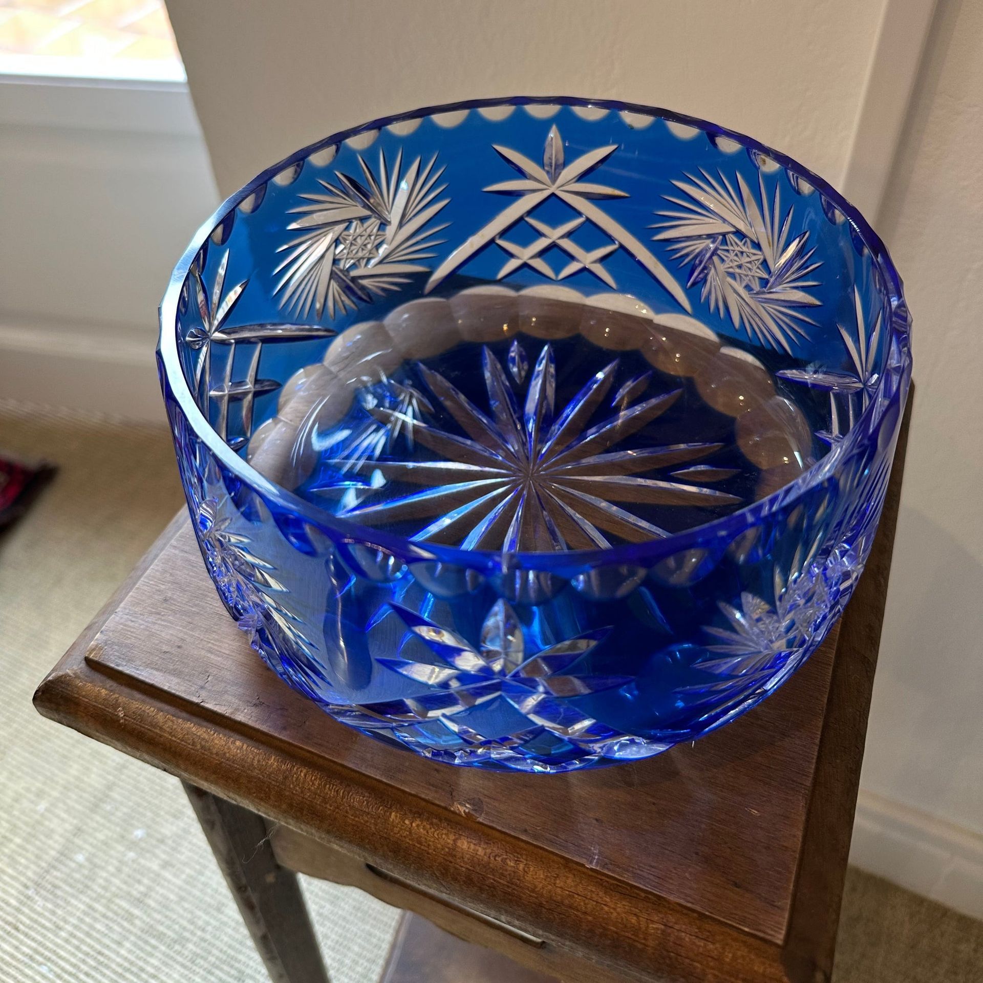 Cuenco de cristal tallado de color azul sobre una pequeña mesa de madera, con patrones intrincados visibles, en el interior.