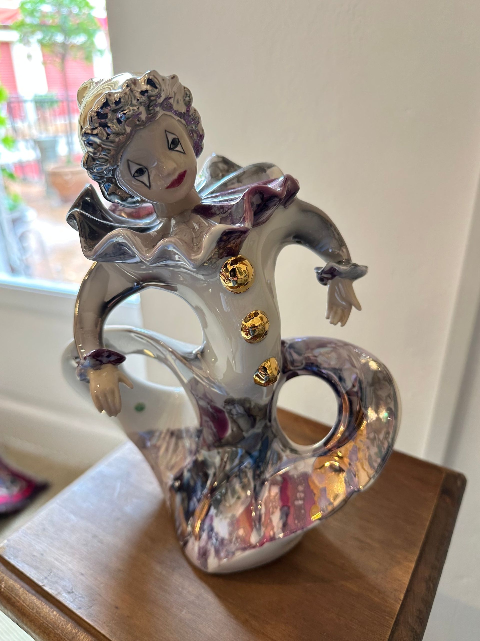 Figura de payaso iridiscente de color blanco y morado con botones dorados, sobre superficie de madera.