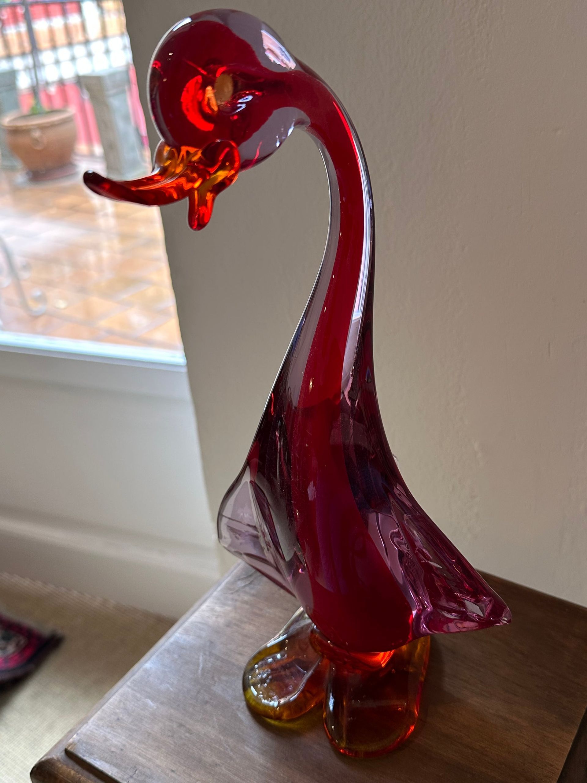 Figura de pato de cristal rojo sobre superficie de madera, situada en el interior.