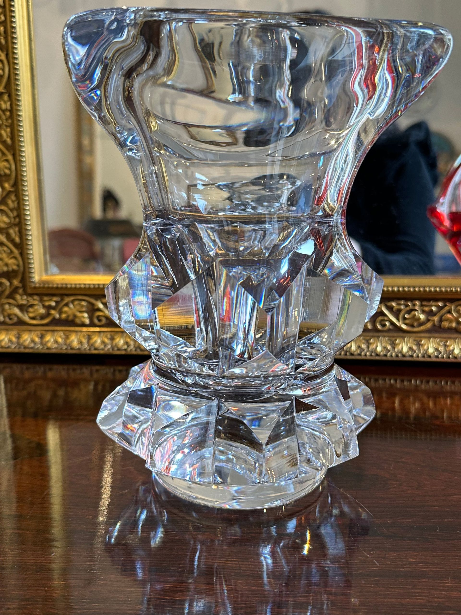 Candelabro de vidrio transparente facetado sobre una superficie de madera con un espejo con marco dorado en el fondo.