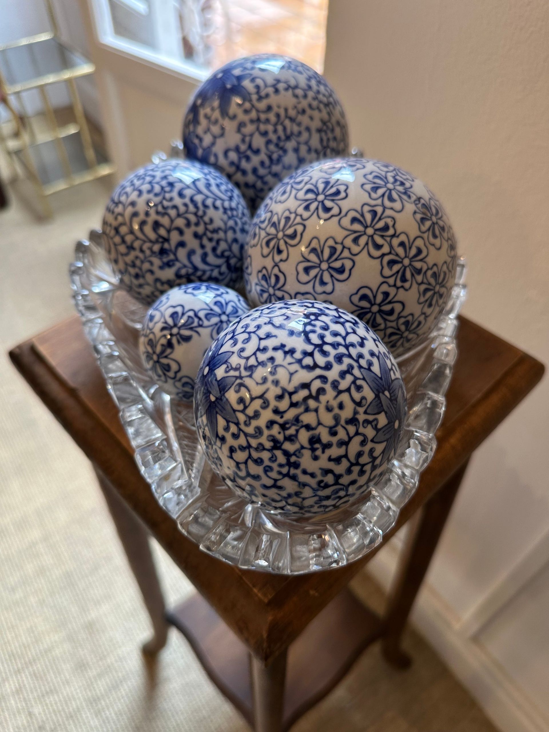 Cinco esferas estampadas en azul y blanco en un plato de vidrio transparente con forma de hoja sobre una pequeña mesa de madera.