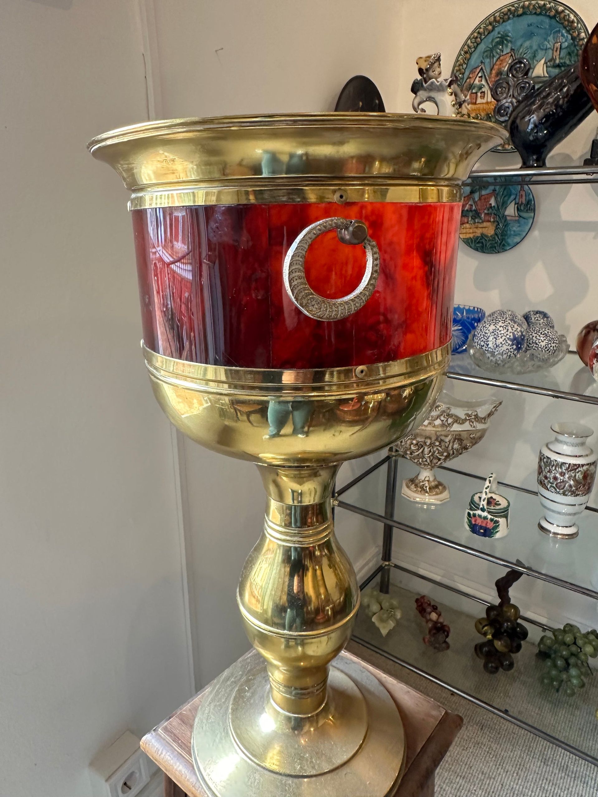 Jarrón de latón y color rojo con emblema de luna creciente, sobre soporte de madera, en una tienda.