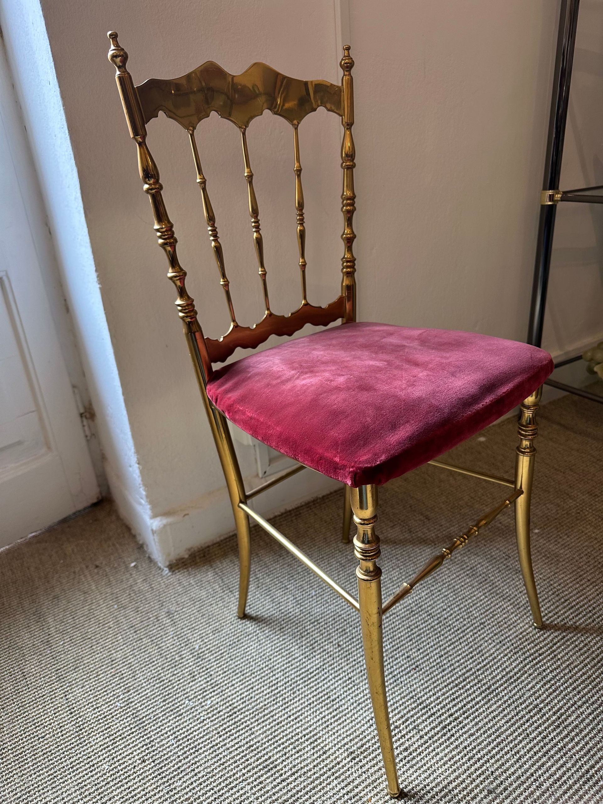 Silla pintada de oro con asiento de terciopelo burdeos contra una pared blanca y una alfombra tejida.