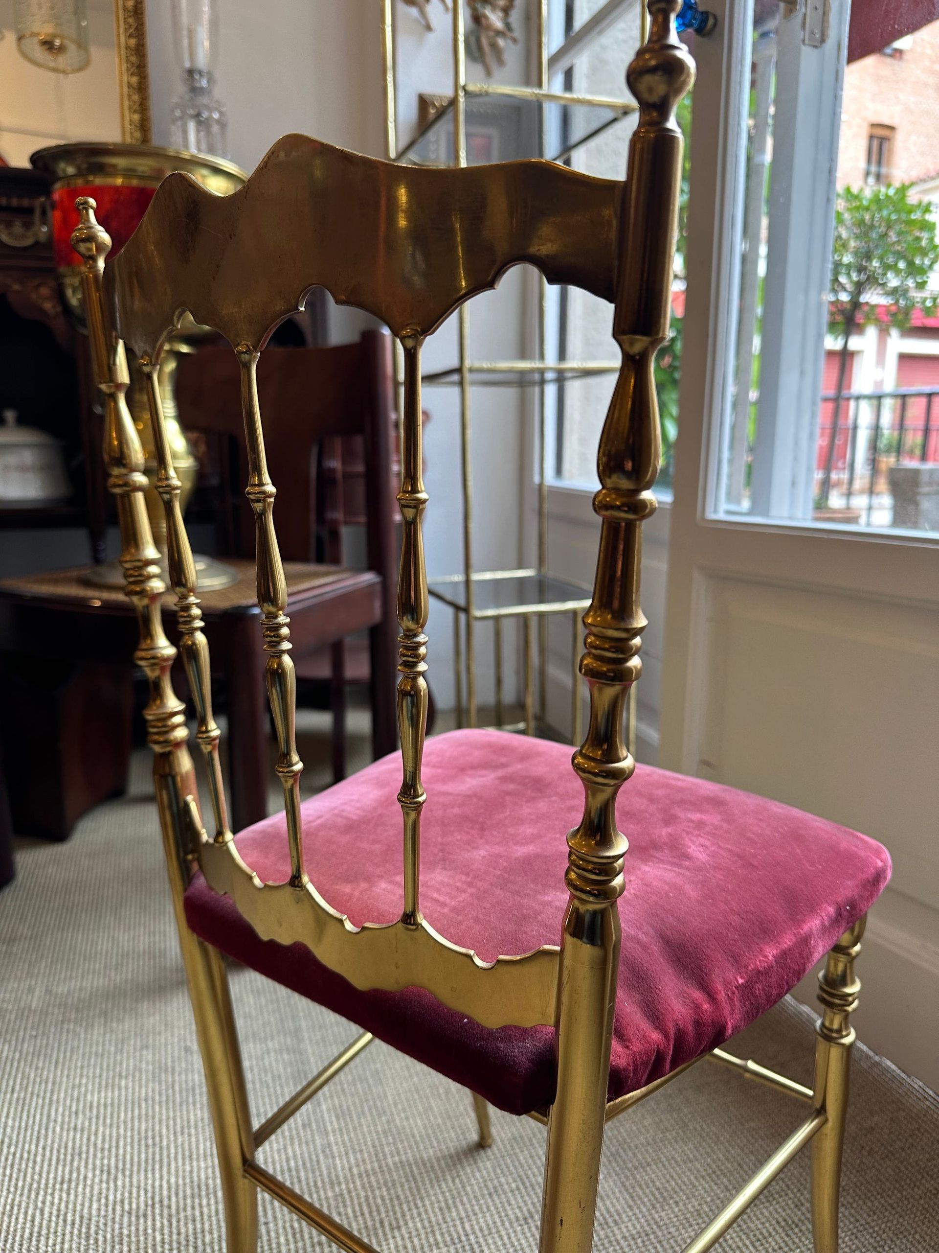 Silla dorada con asiento rojo afelpado. En una habitación con ventana, posiblemente un comedor.