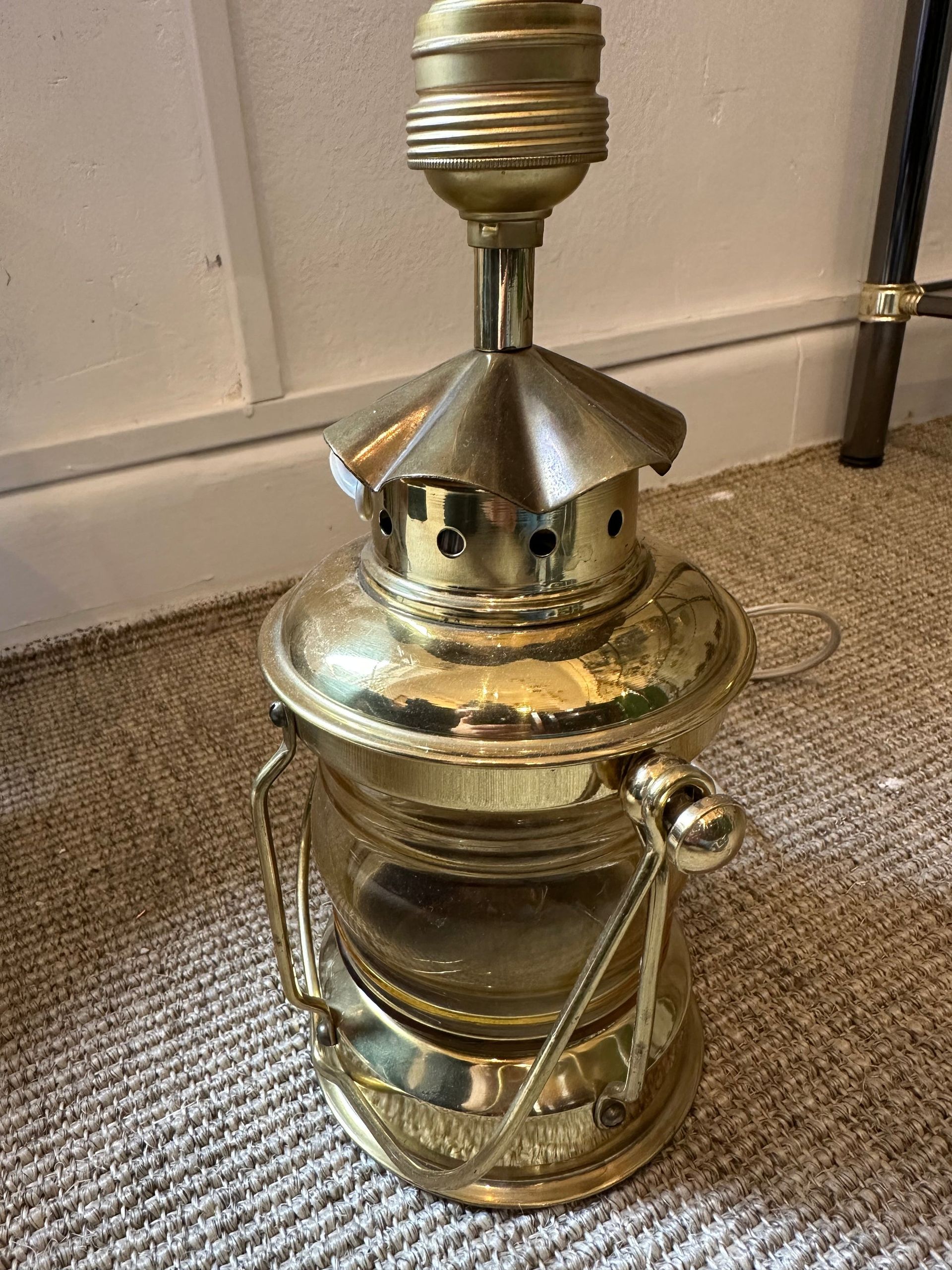 Lámpara de farol de latón con portalámparas sobre alfombra de color neutro.