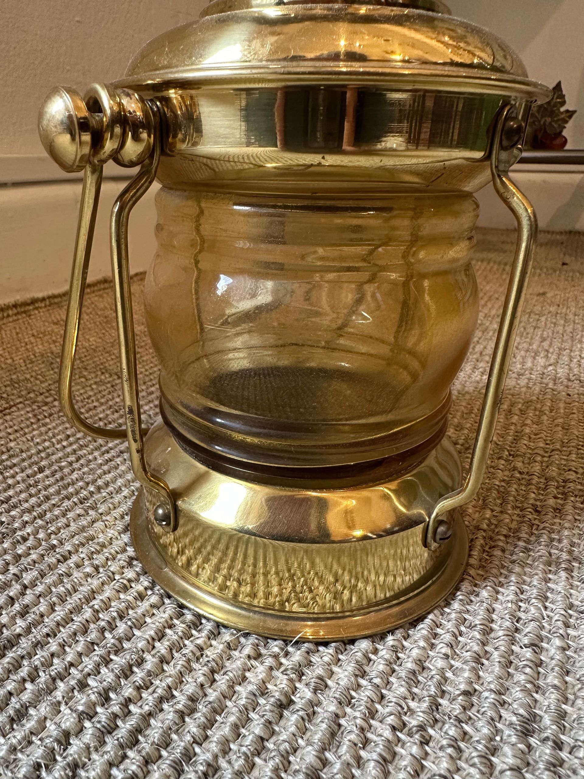 Farol de latón con cristal color ámbar, sobre alfombra beige.