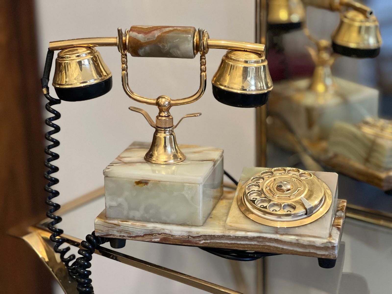 Teléfono vintage de oro y ónix sobre estante, con cable negro enrollado.