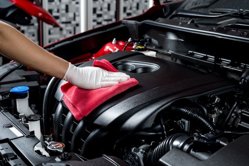 Persona que lleva un guante limpiando el motor de un coche negro con un paño rojo.