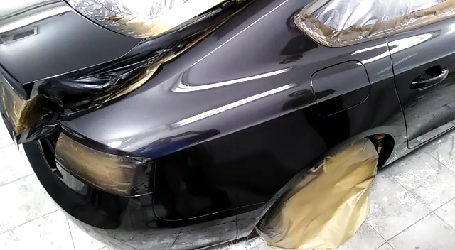 Coche negro siendo pintado, cubierto con plástico y papel, dentro de un taller.