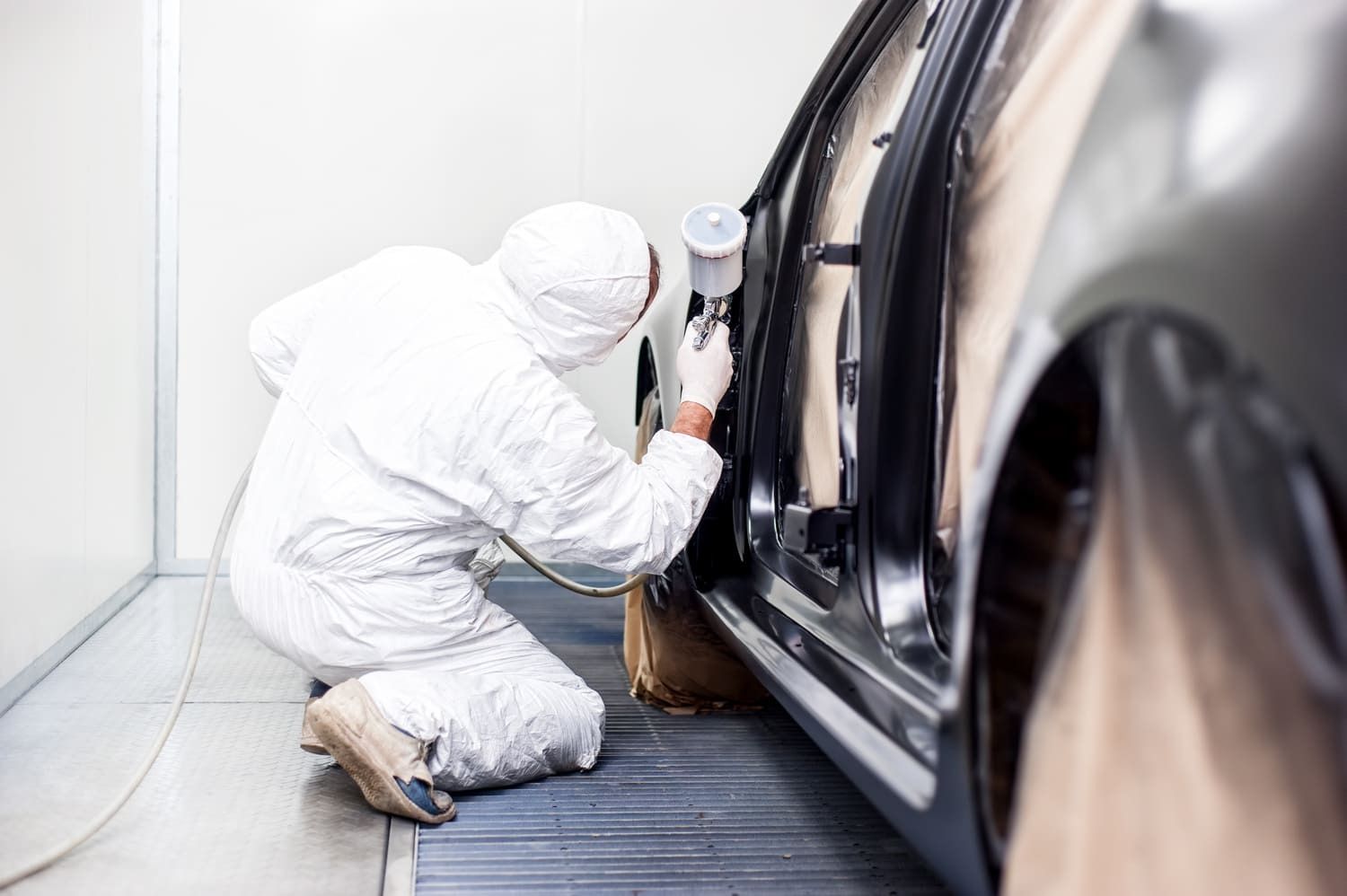 Persona con traje de protección blanco pulveriza pintura en la puerta de un coche en un taller.