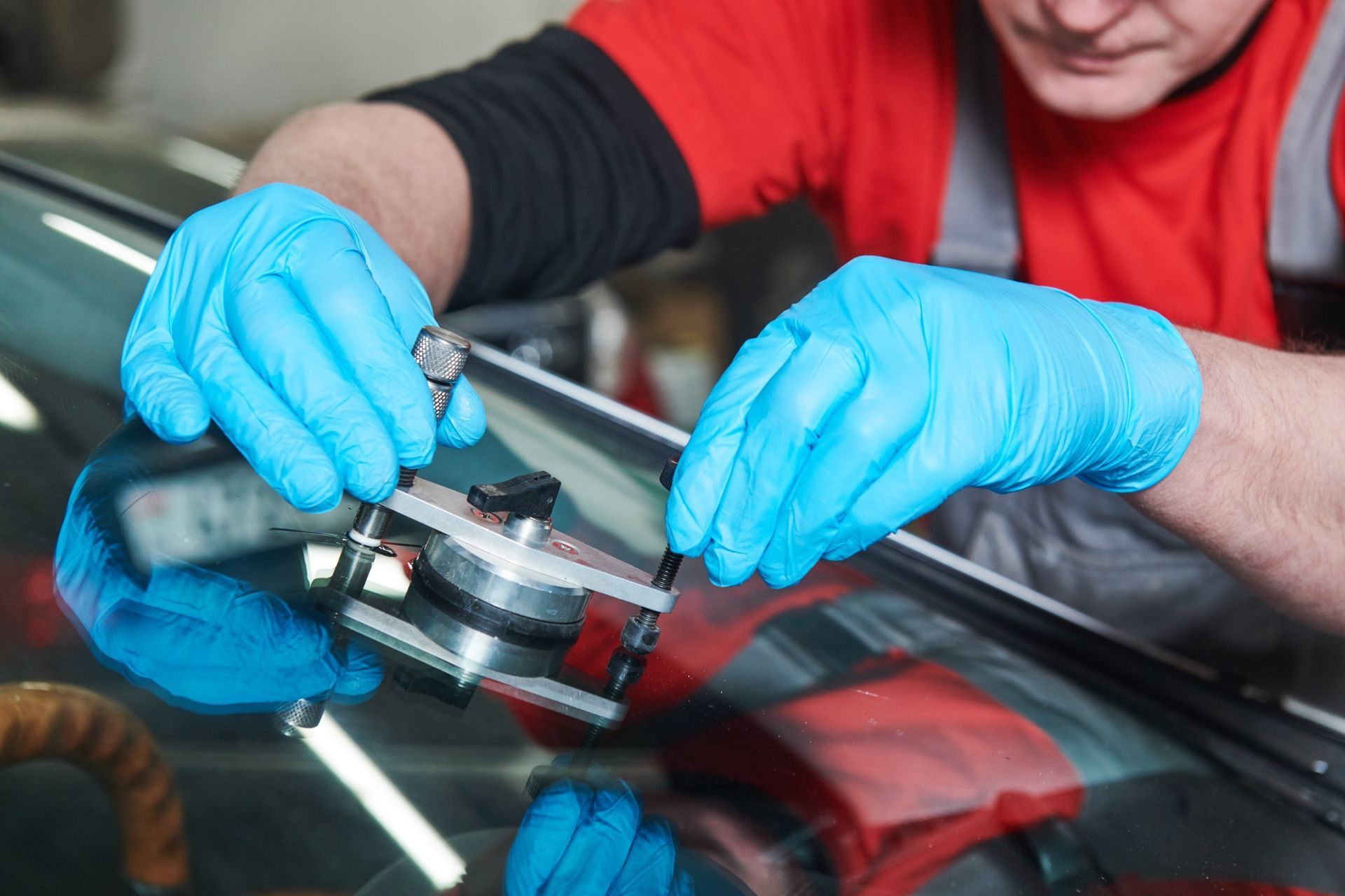 Un mecánico con guantes azules repara una grieta en el parabrisas con equipo especializado, probablemente en un taller de reparación de automóviles.