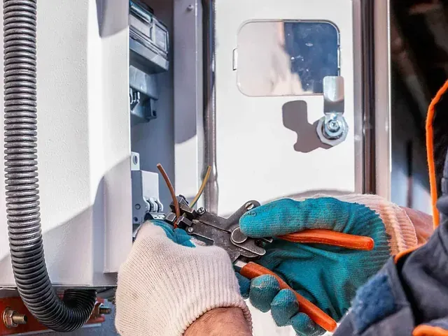 Un electricista está trabajando en una caja eléctrica con alicates.